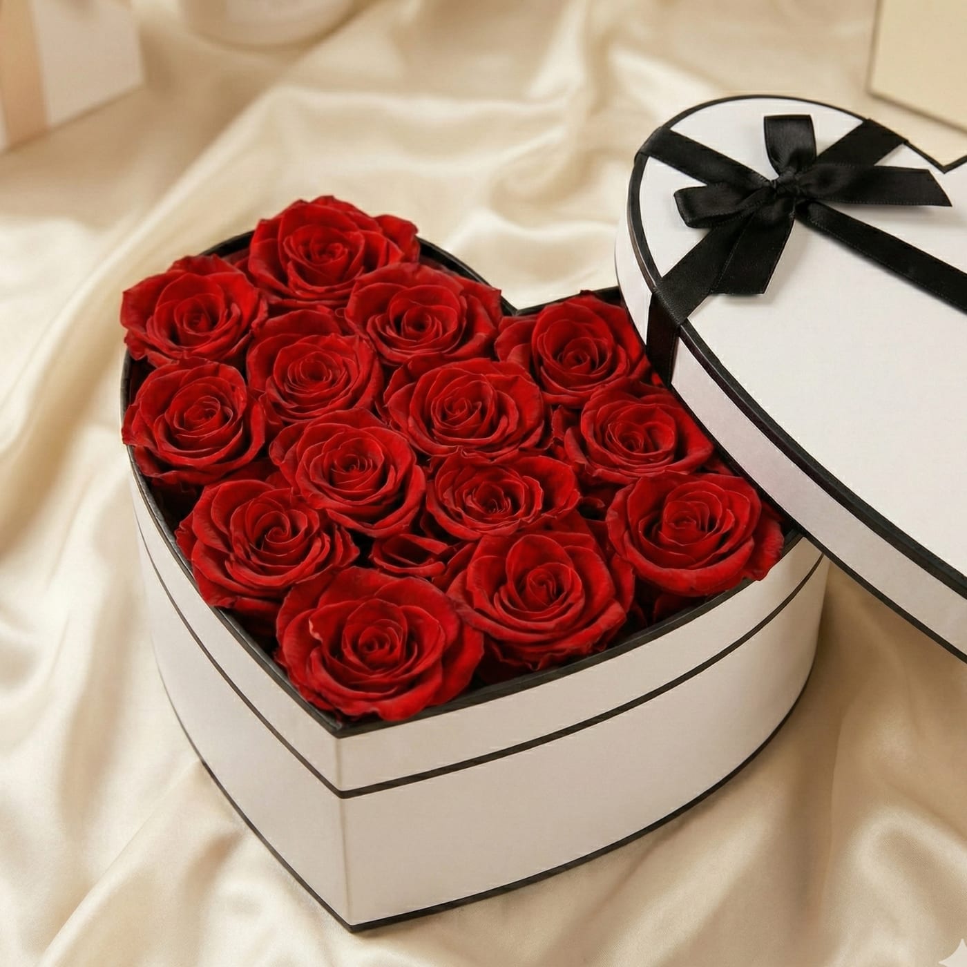 Heart-shaped white box filled with red roses, with a black-ribboned lid beside it.