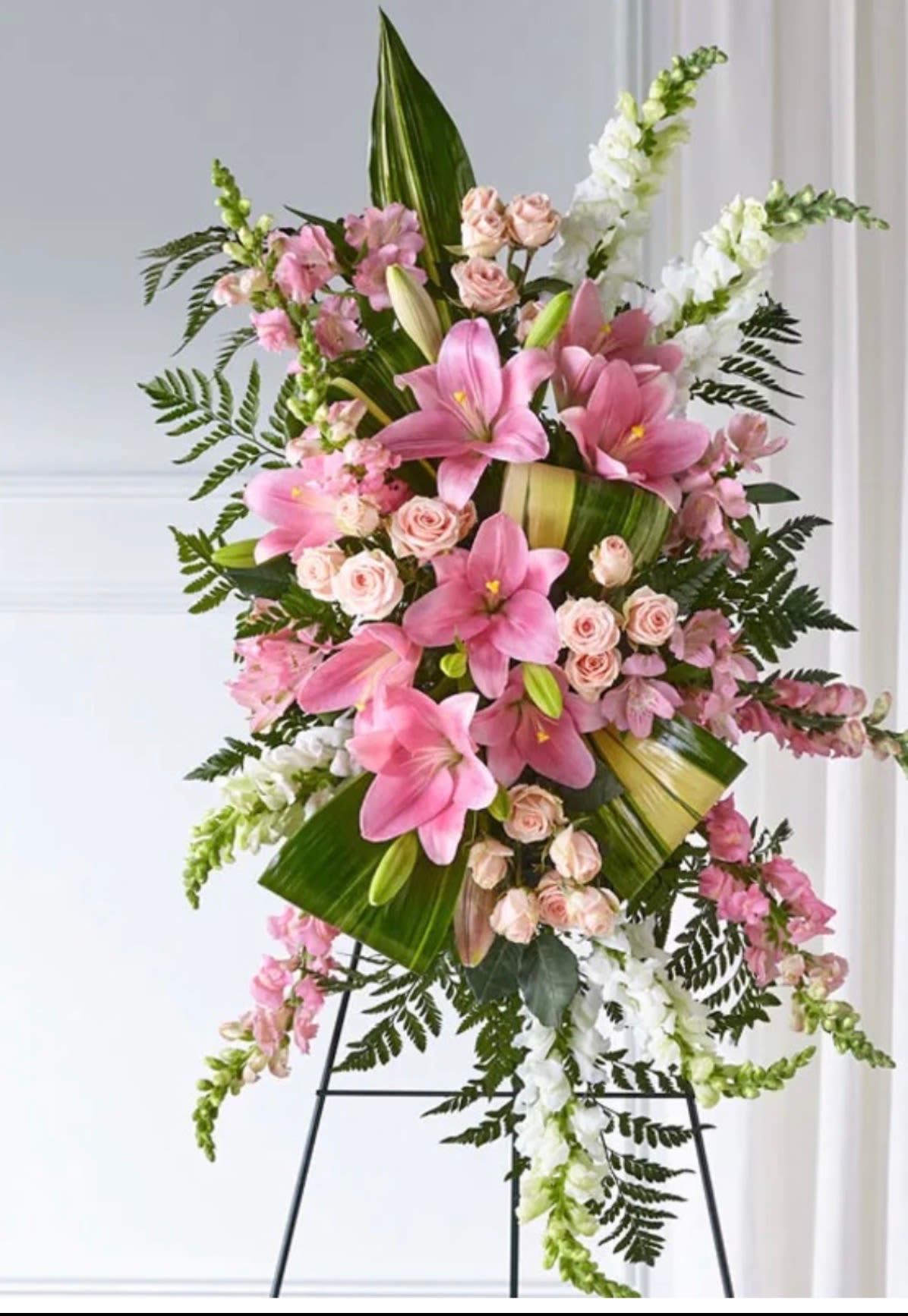 ELEGANT EMBRACE STANDING SPRAY - Our Elegant Embrace  Standing Spray shares the warmth and comfort your loved ones need during this difficult time through each blushing bloom. A local florist beautifully combines lilies, spray roses and snapdragons with greens to express your heartfelt love.  