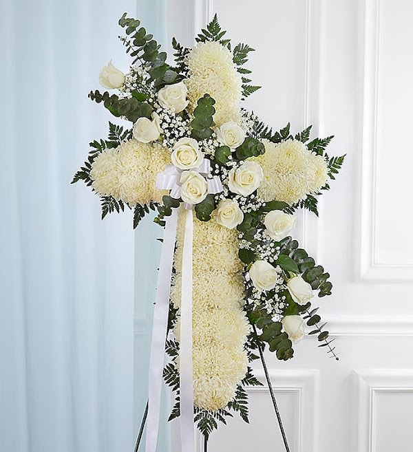 Standing cross of white flowers with white roses and ribbon on an easel