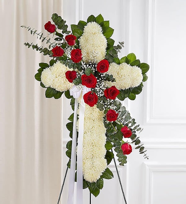 Standing cross of white flowers with red roses and ribbon on an easel