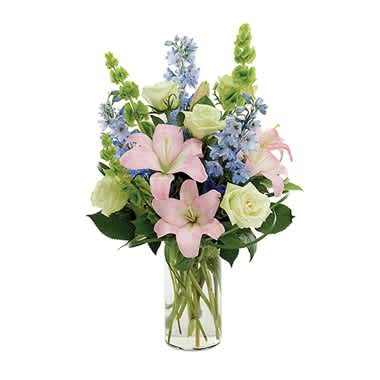 A Day At The Beach - You can practically hear the waves crashing and almost feel a gentle breeze caressing your face. This bounty of nature’s beauty boasts green roses, blue delphinium, pink Asiatic lilies, Bell of Ireland and lily grass in an elegant clear cylinder vase. 