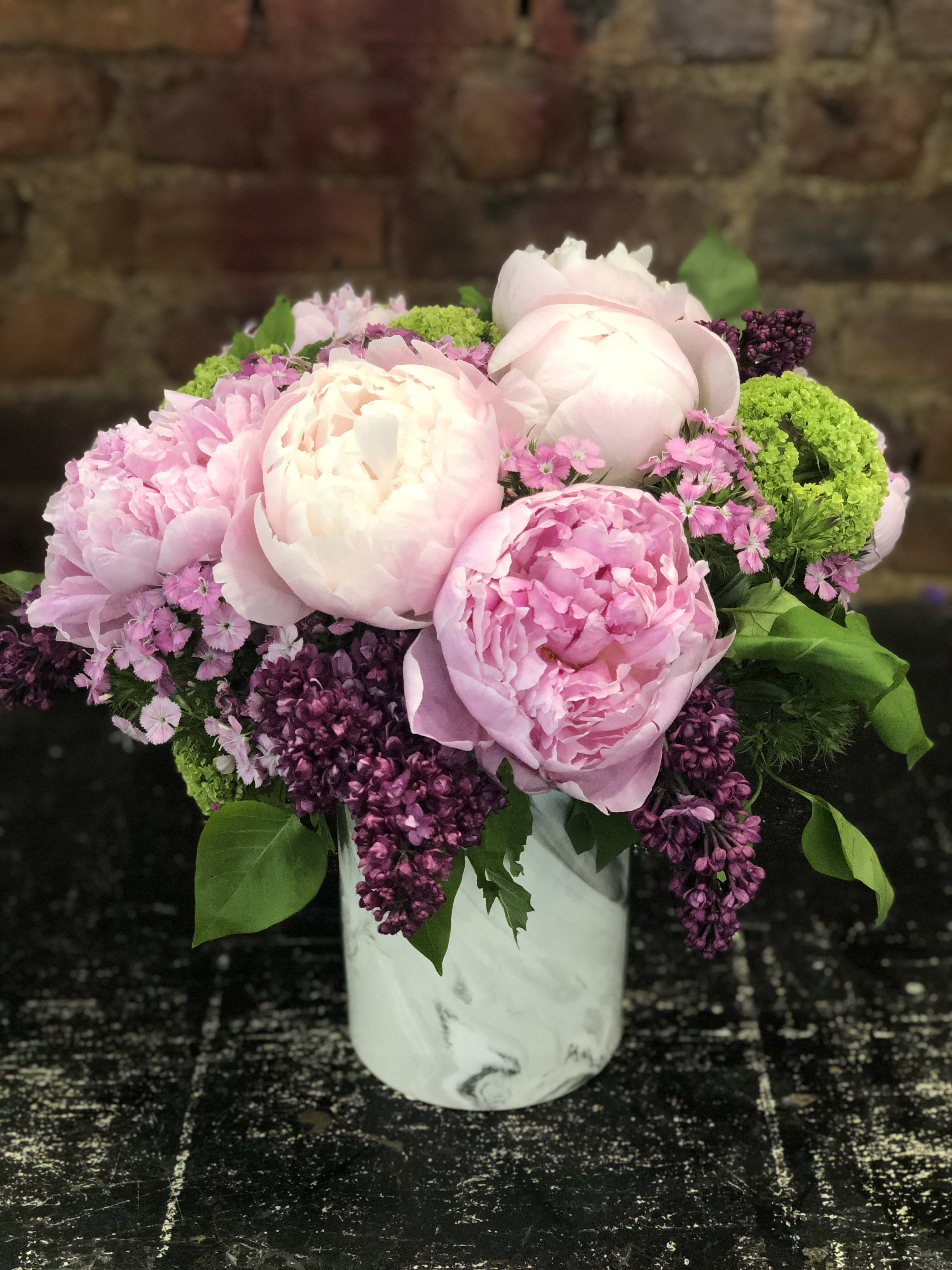 Pink peonies and purple blooms arranged in a white vase