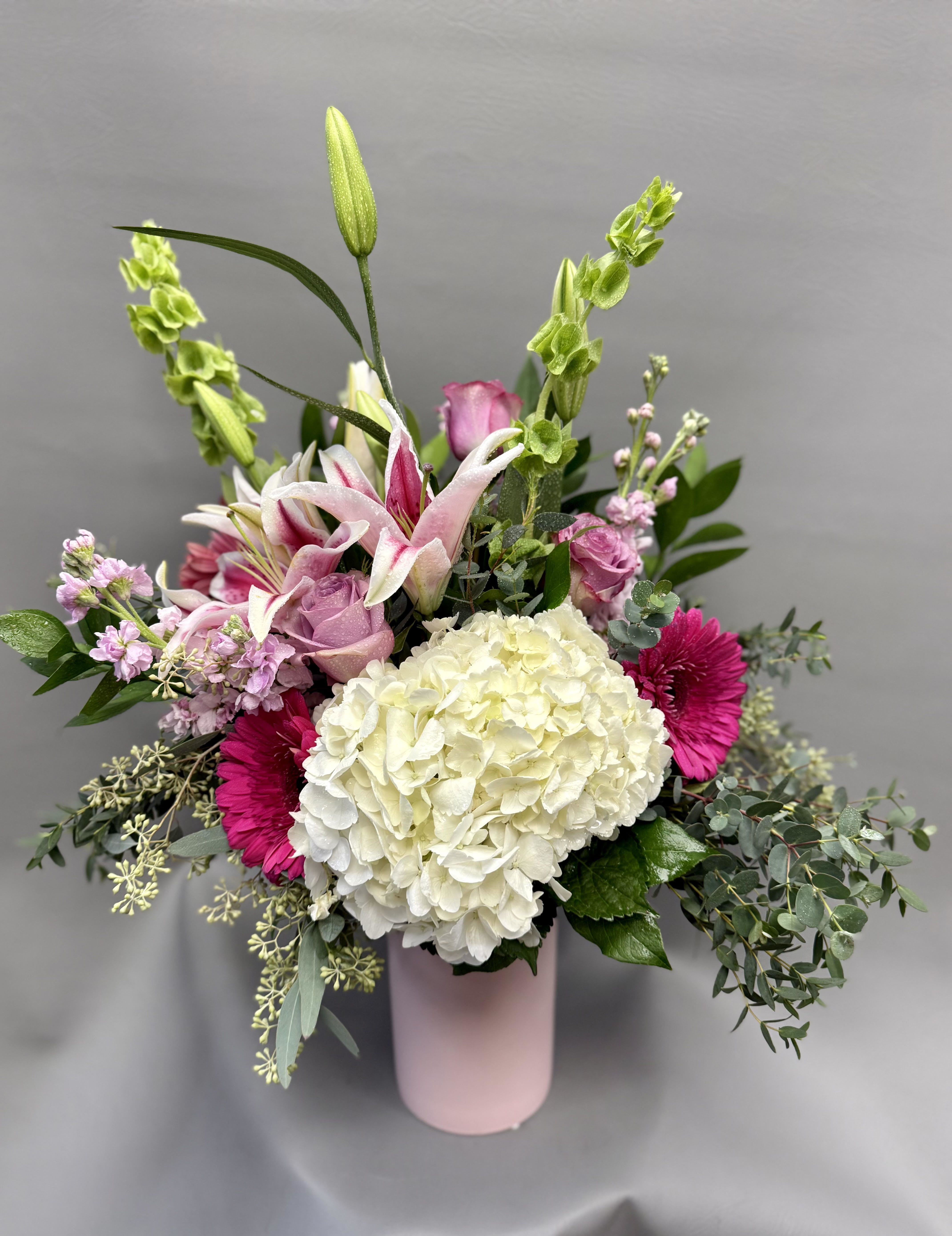 Tall pink and white mixed flower arrangement with hydrangea, lilies, and gerbera daisies in a pink vase