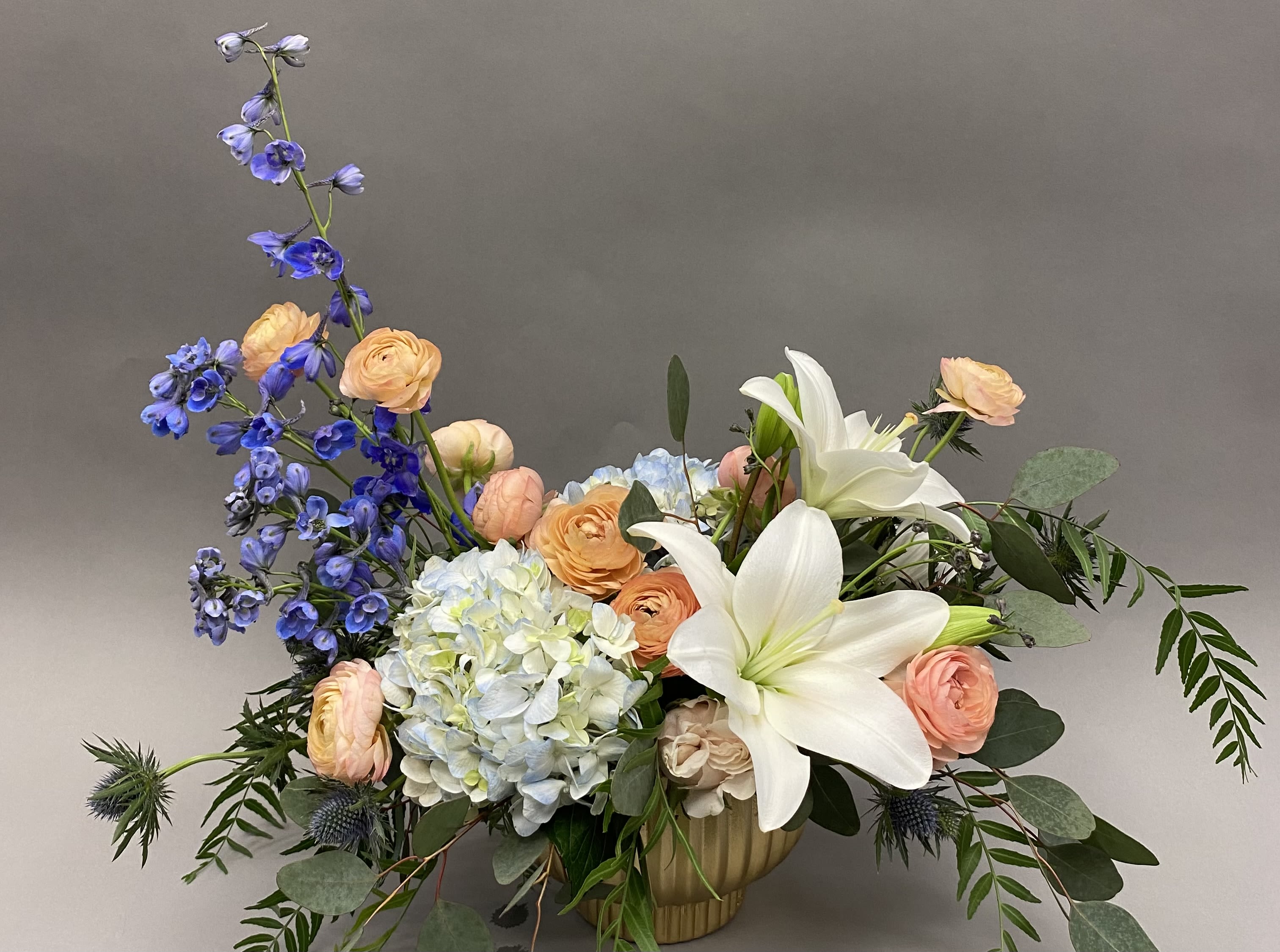 Mixed bouquet with white lilies, blue delphinium, peach ranunculus, and pale hydrangea