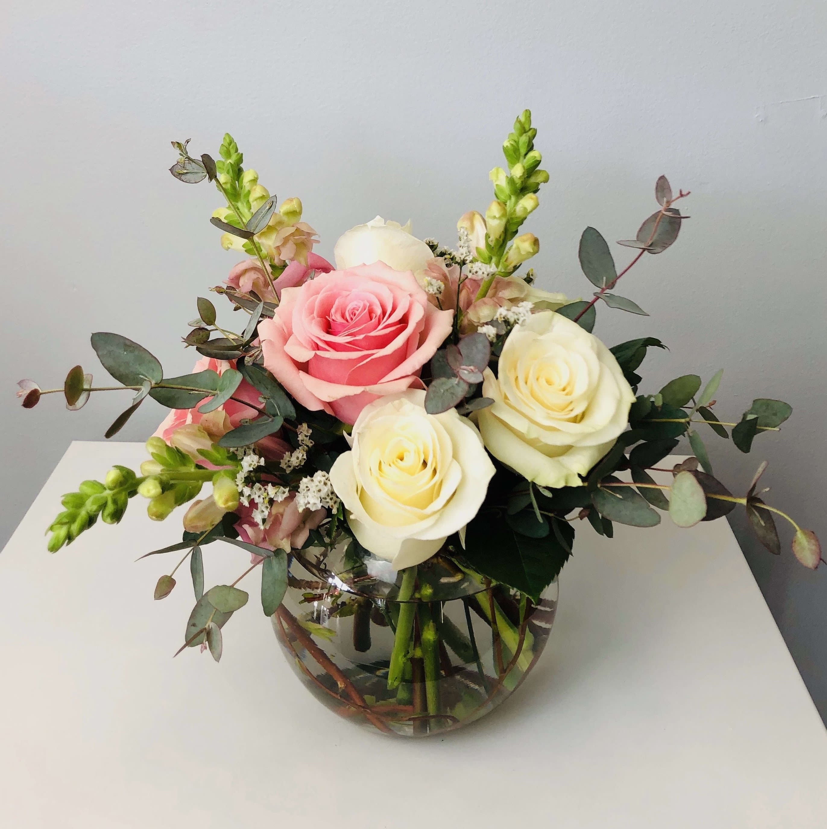 Sweet and Subtle  - Blush pink roses and creamy white roses are accented with  snapdragons or stock with eucalyptus in a clear bowl. Sweet &amp; Subtle is the perfect gift for a birthday, thank you, or just because.   Approximately 10" Tall  Container Country of Origin: USA Flower Country of Origin: Canada, Ecuador, Columbia