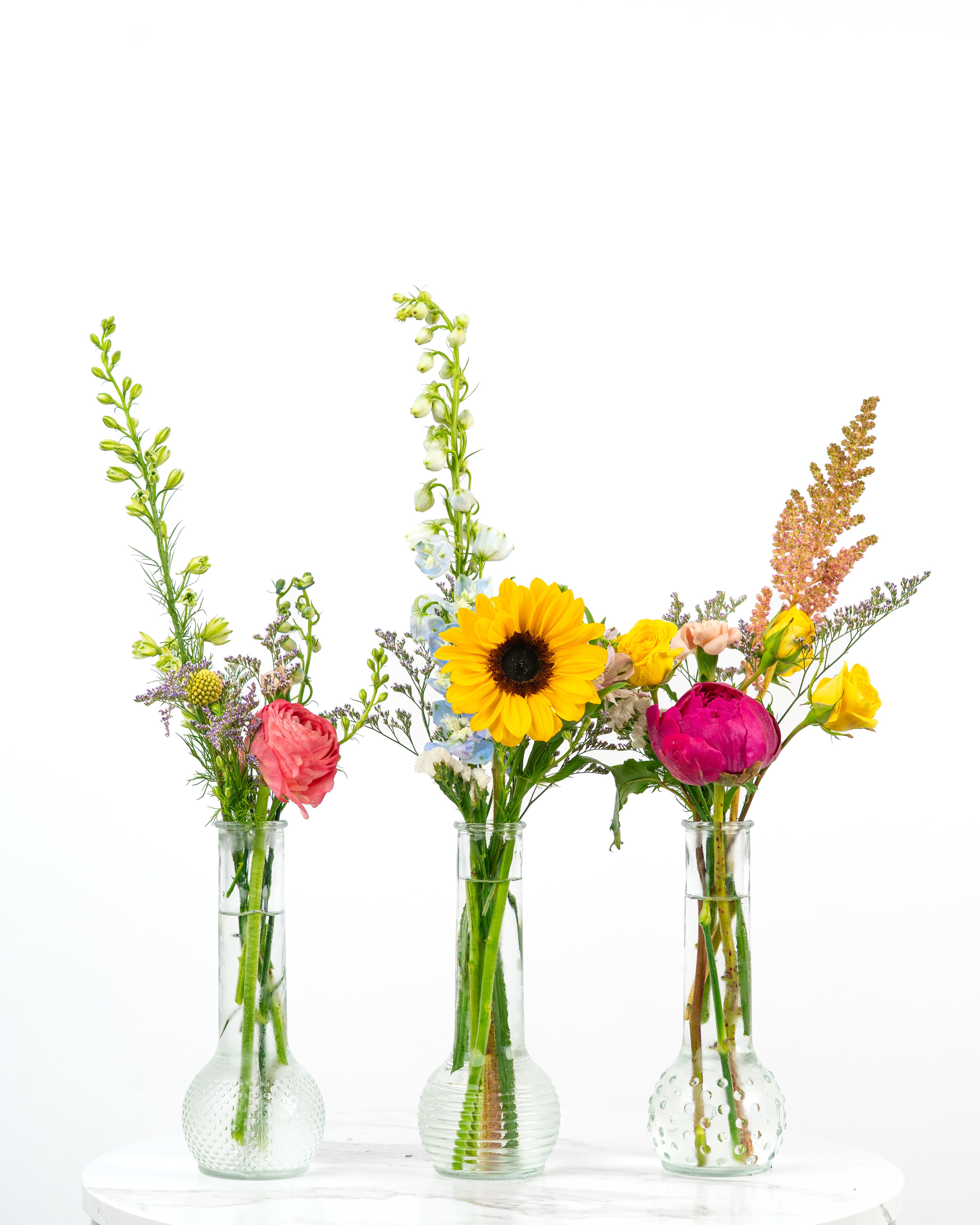 Three small flower arrangements in clear glass vases with bright mixed blooms
