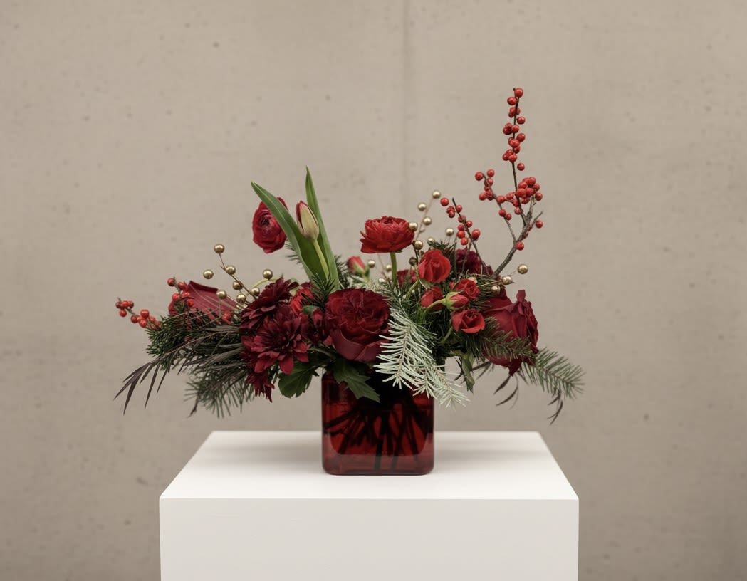 Red floral arrangement in a square glass vase with berries and greenery
