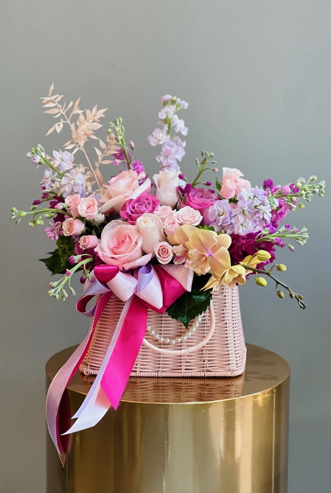 Pink and lavender floral arrangement in a woven basket with ribbon