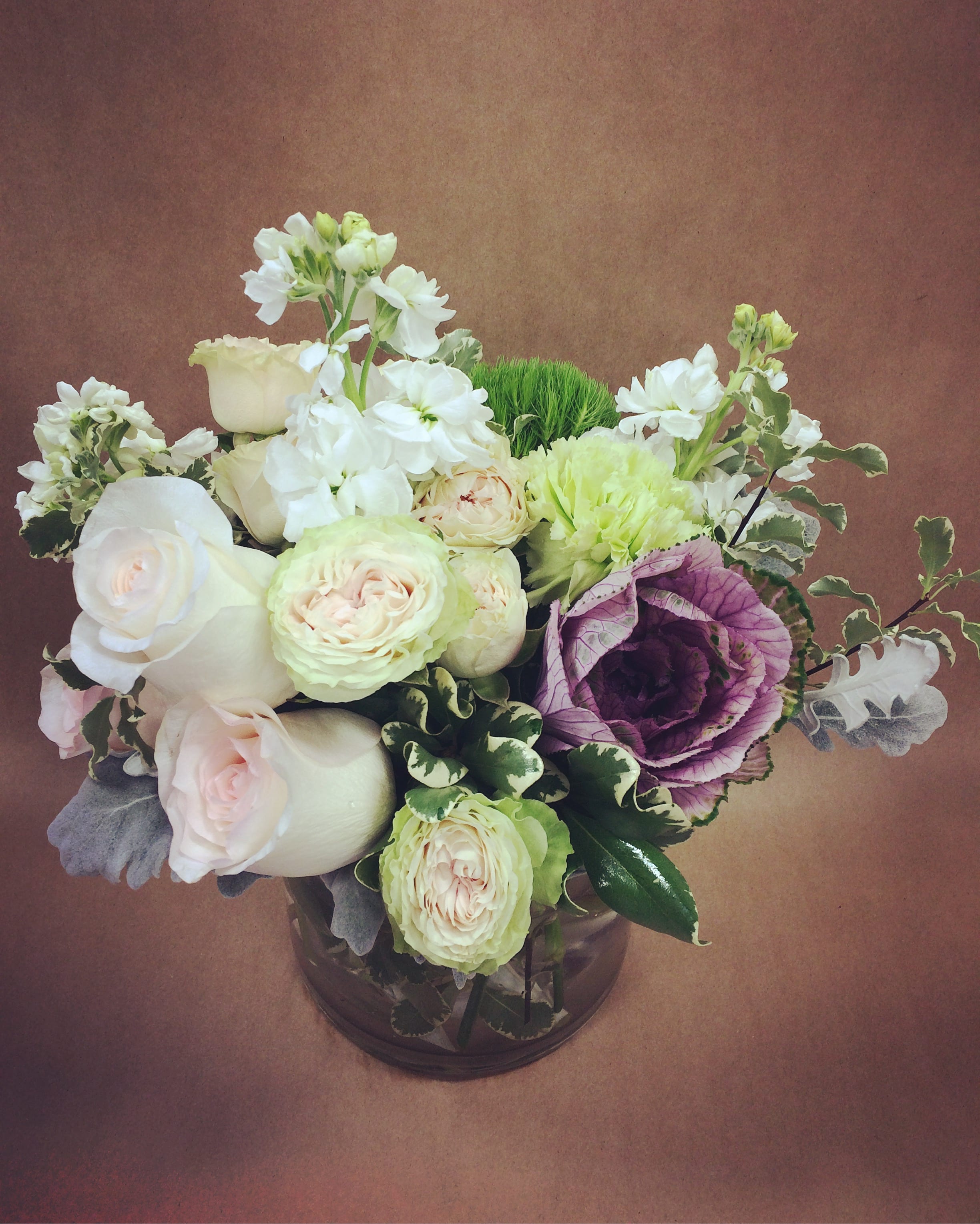 White and pale pink roses with purple cabbage in a glass vase