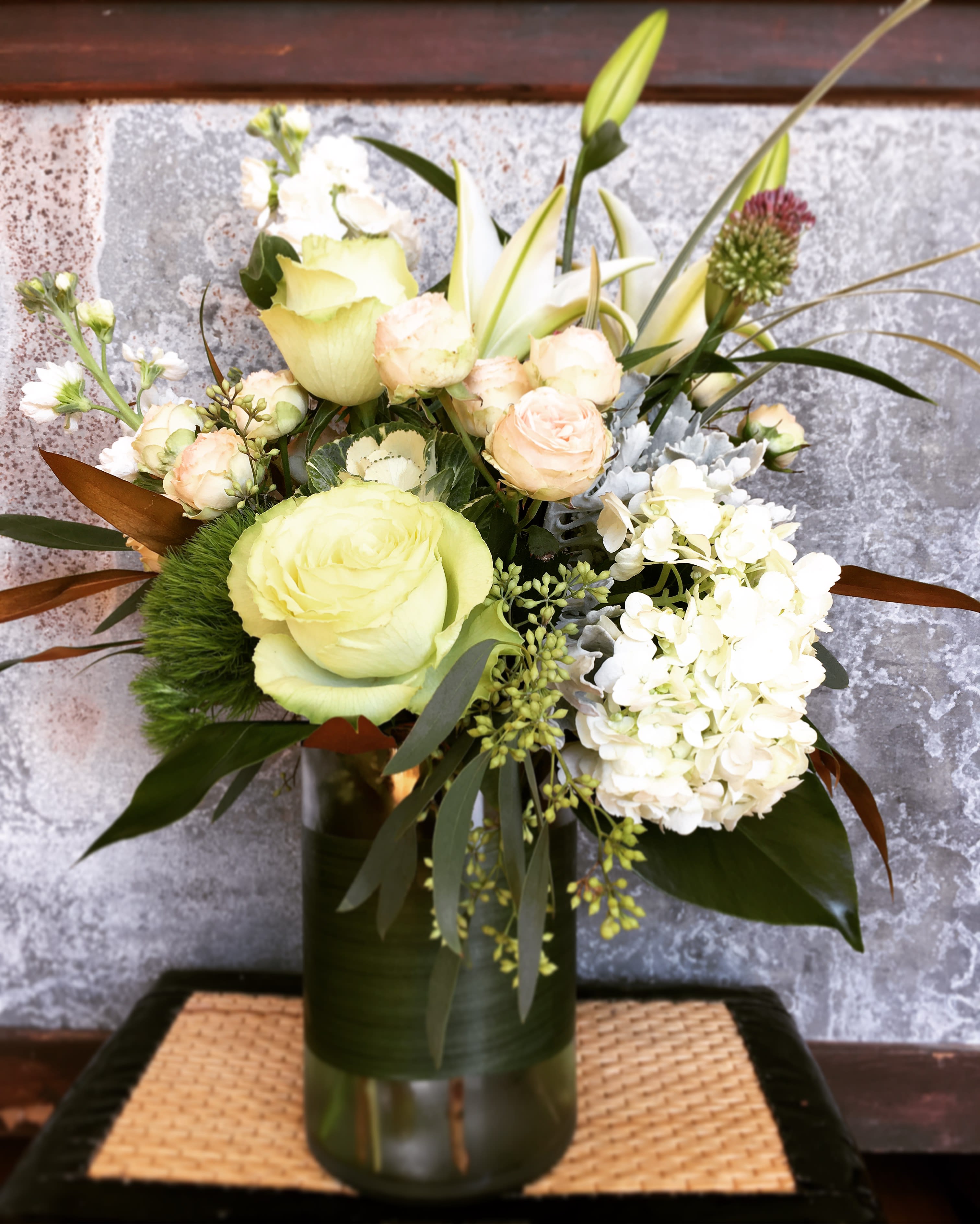 Mixed bouquet of pale roses, lilies, and white hydrangea in a glass vase