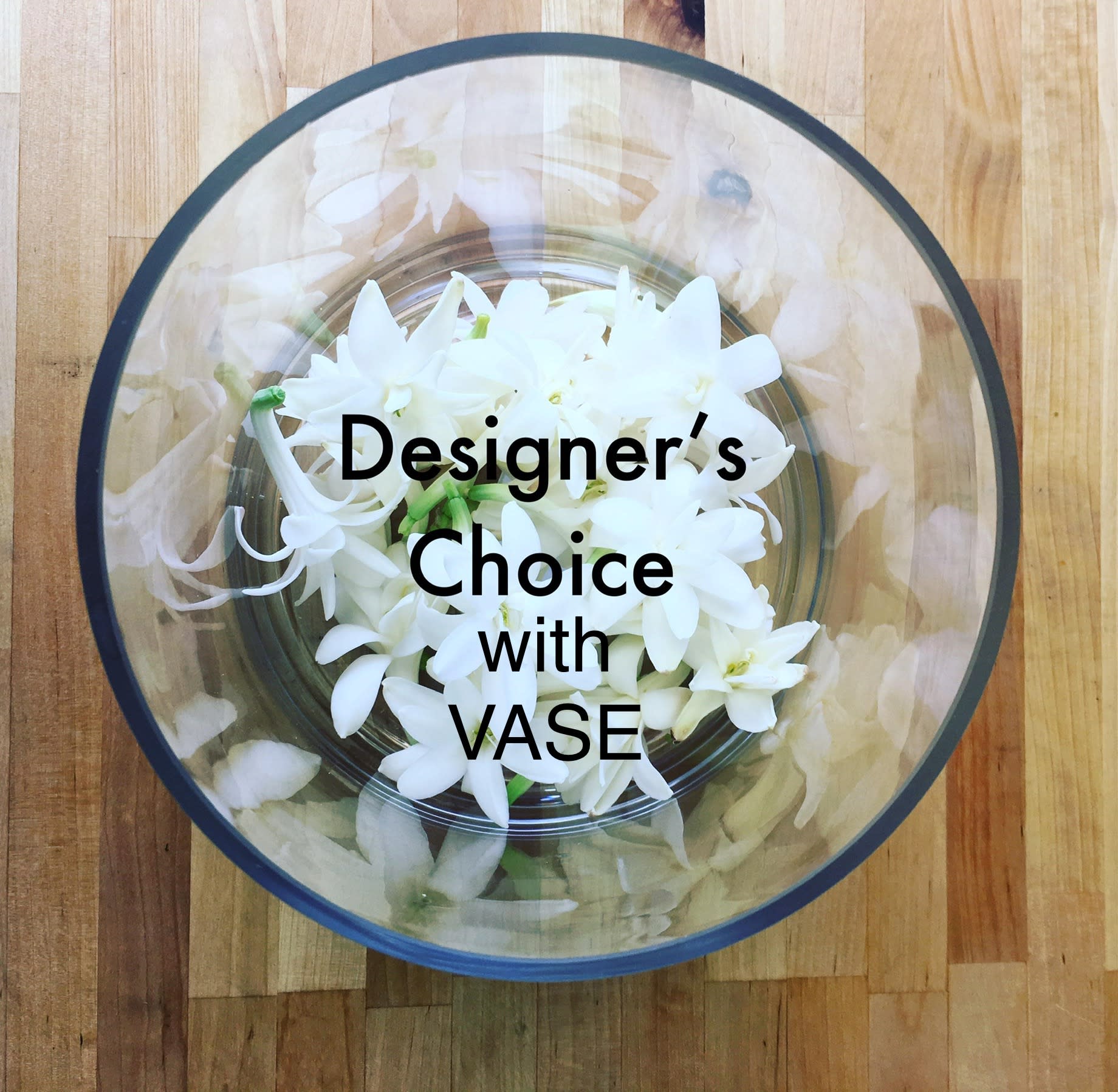 Round glass bowl filled with small white flowers viewed from above on a wooden surface.