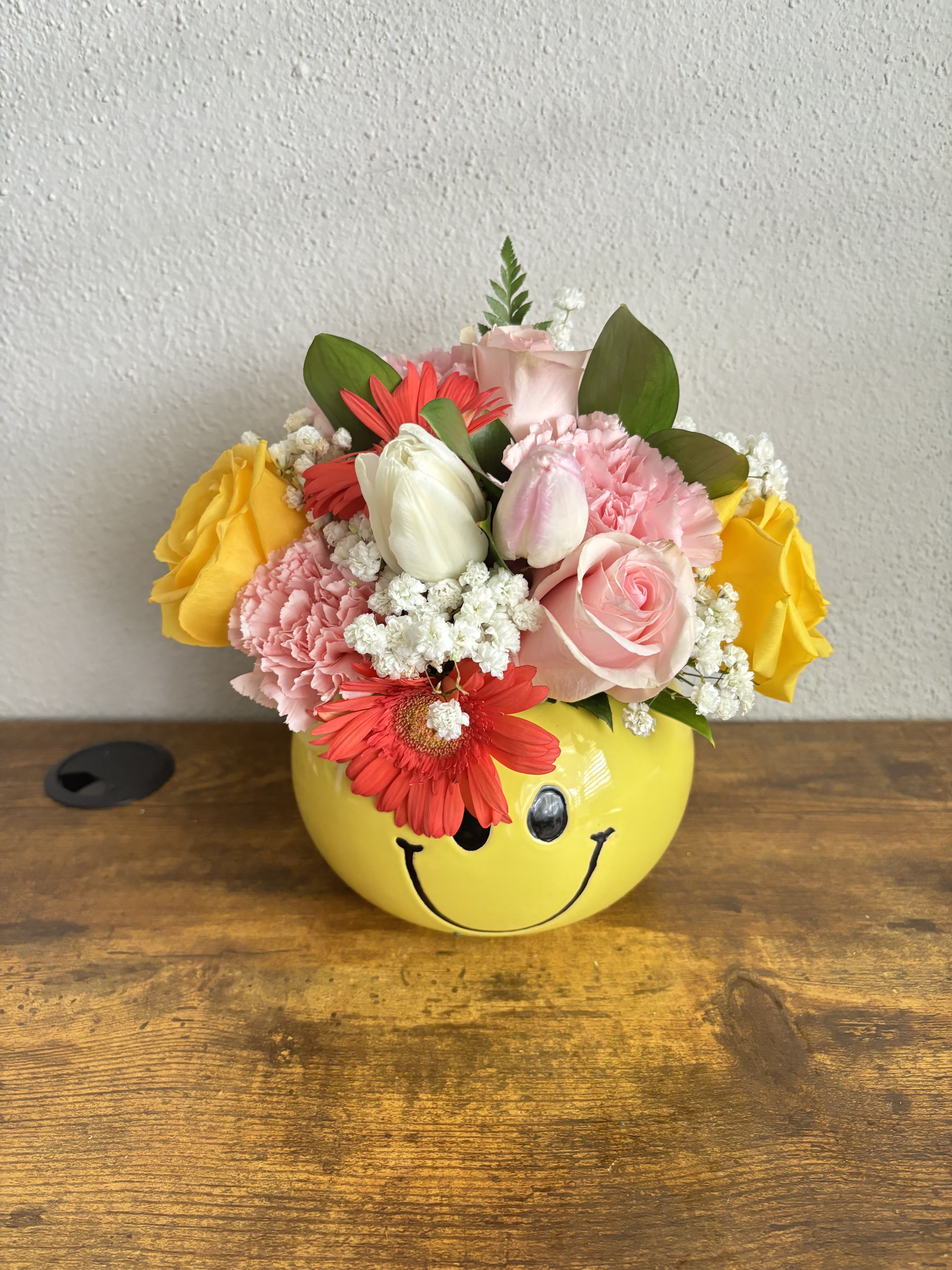 Pink and yellow flower arrangement in a smiley-face pot