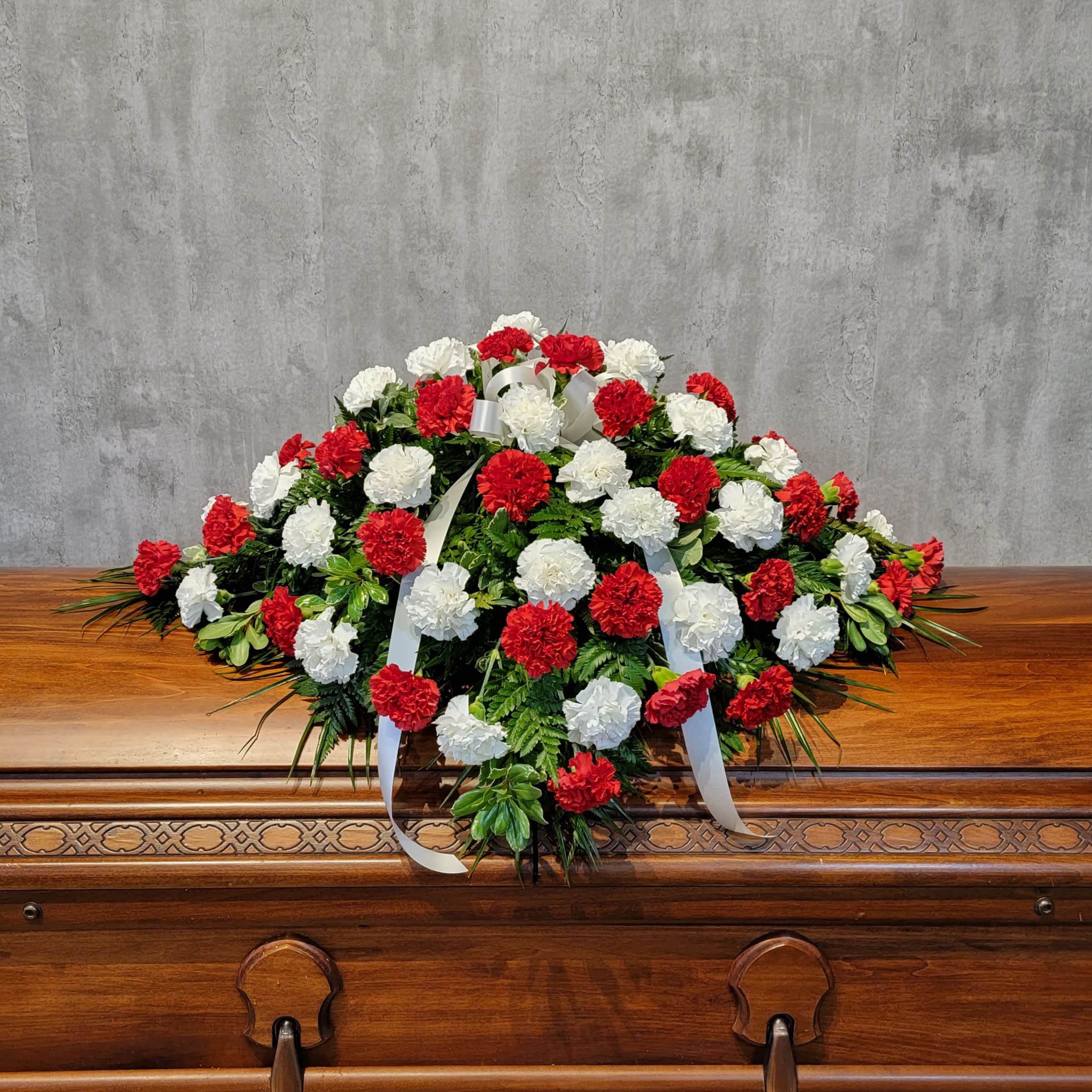 Red and white carnation casket spray with white ribbon on a wooden casket