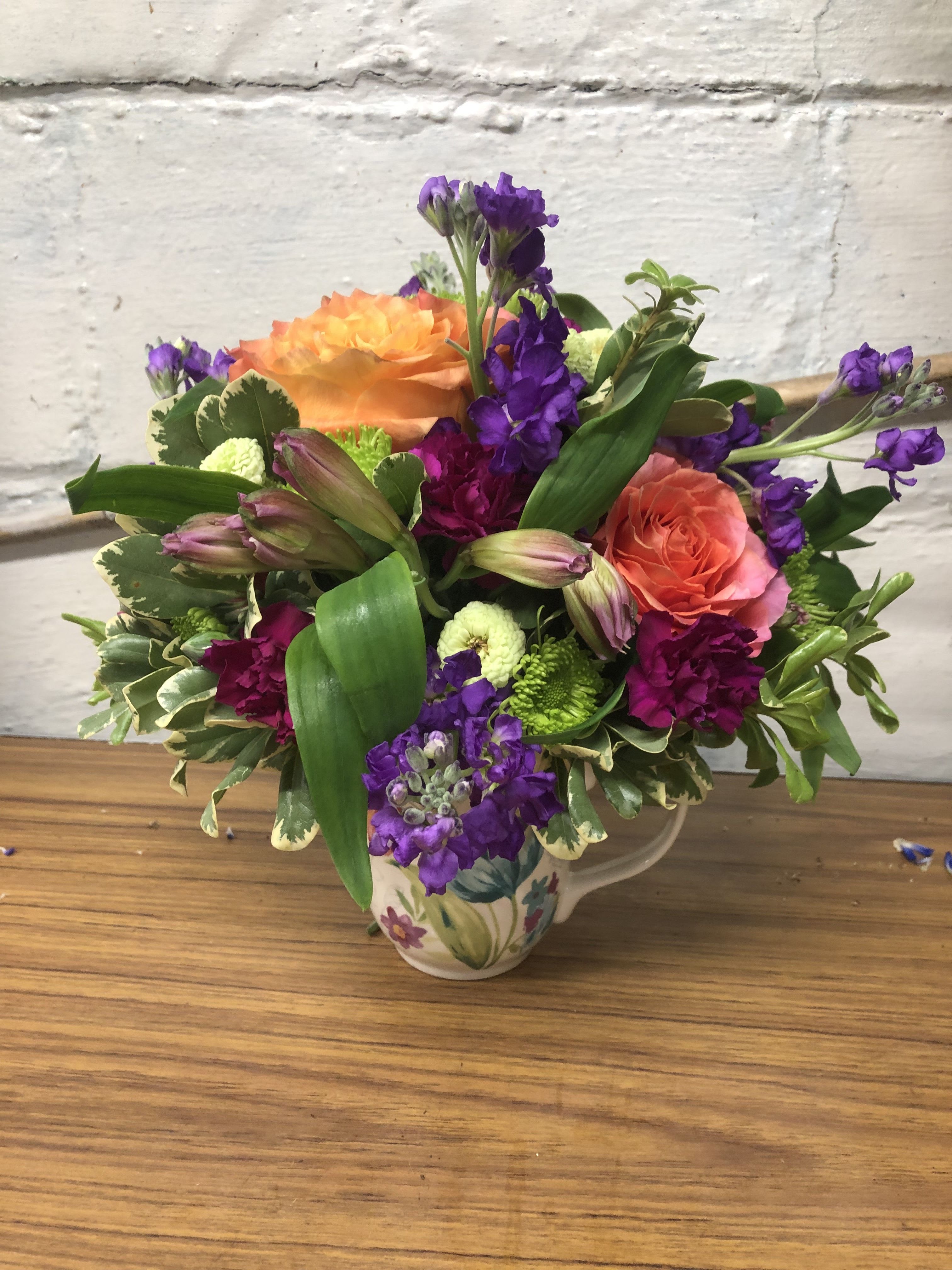 Colorful bouquet of orange and purple flowers in a floral ceramic pitcher