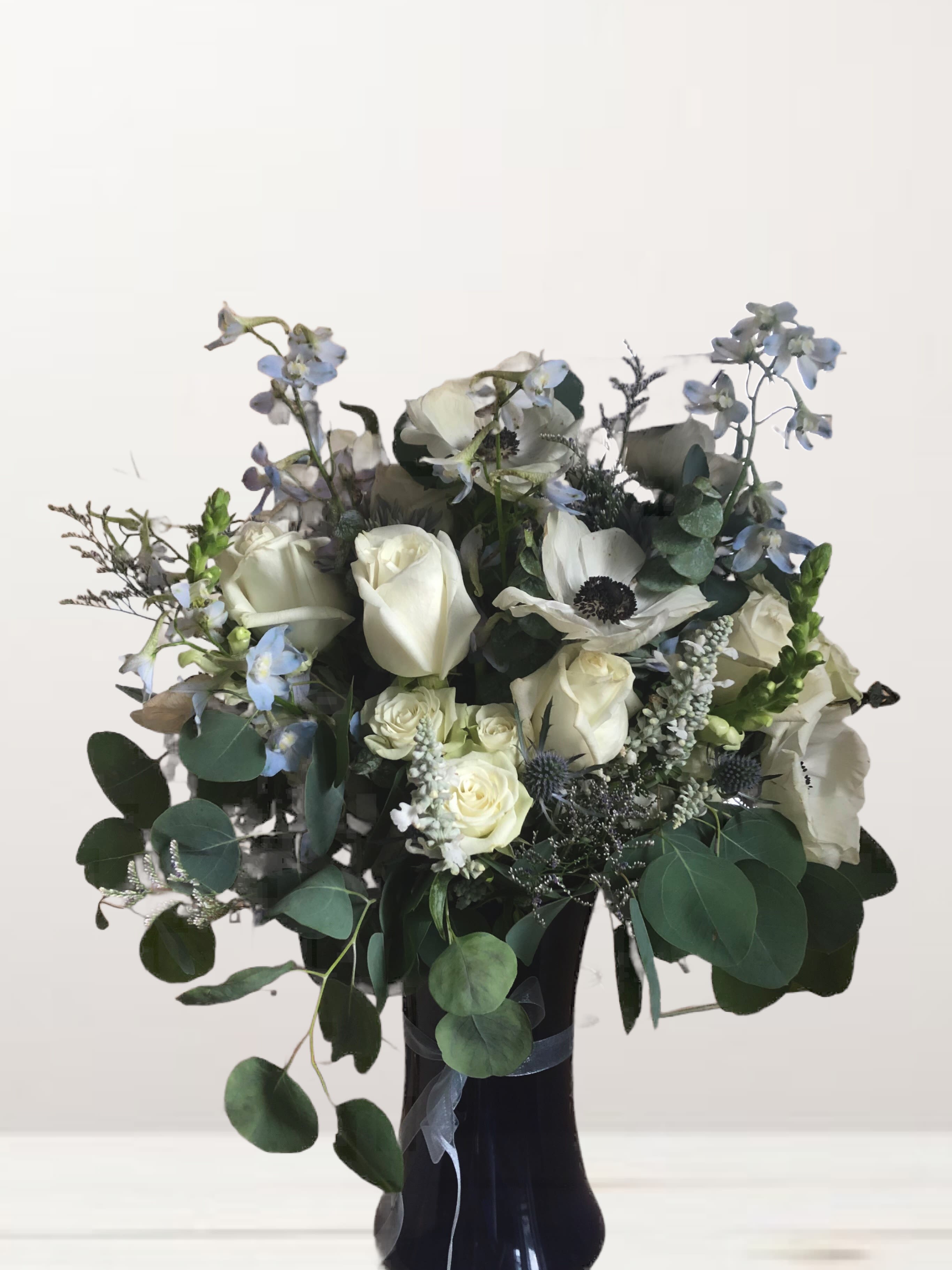 White roses and pale blue flowers in a black vase