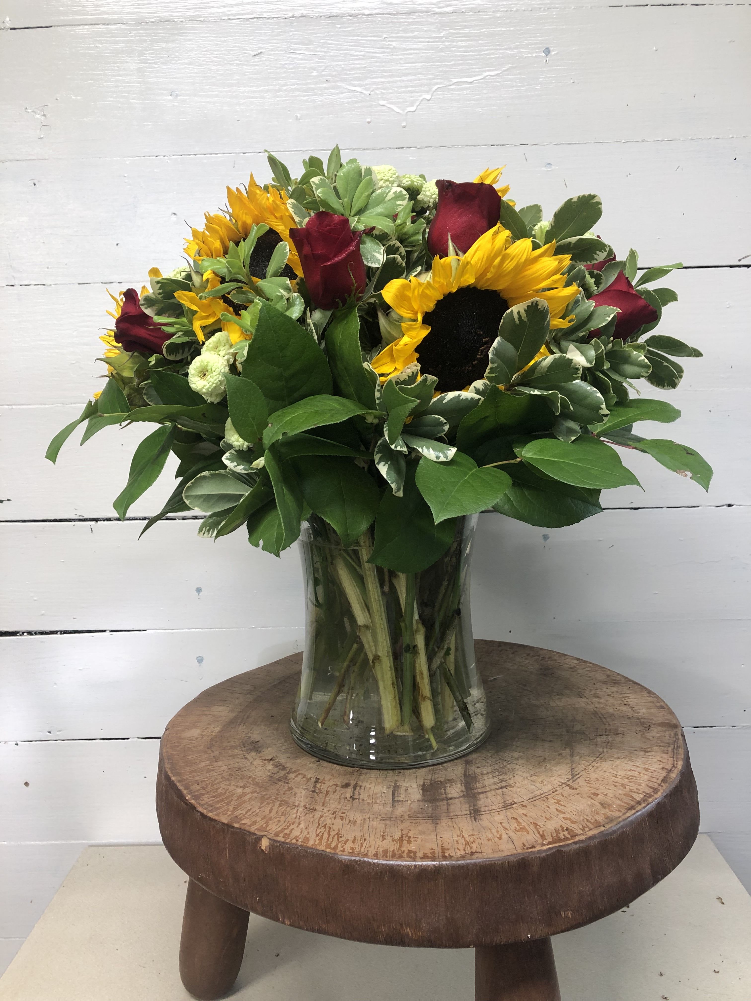 Sunflowers and red roses arranged in a clear glass vase