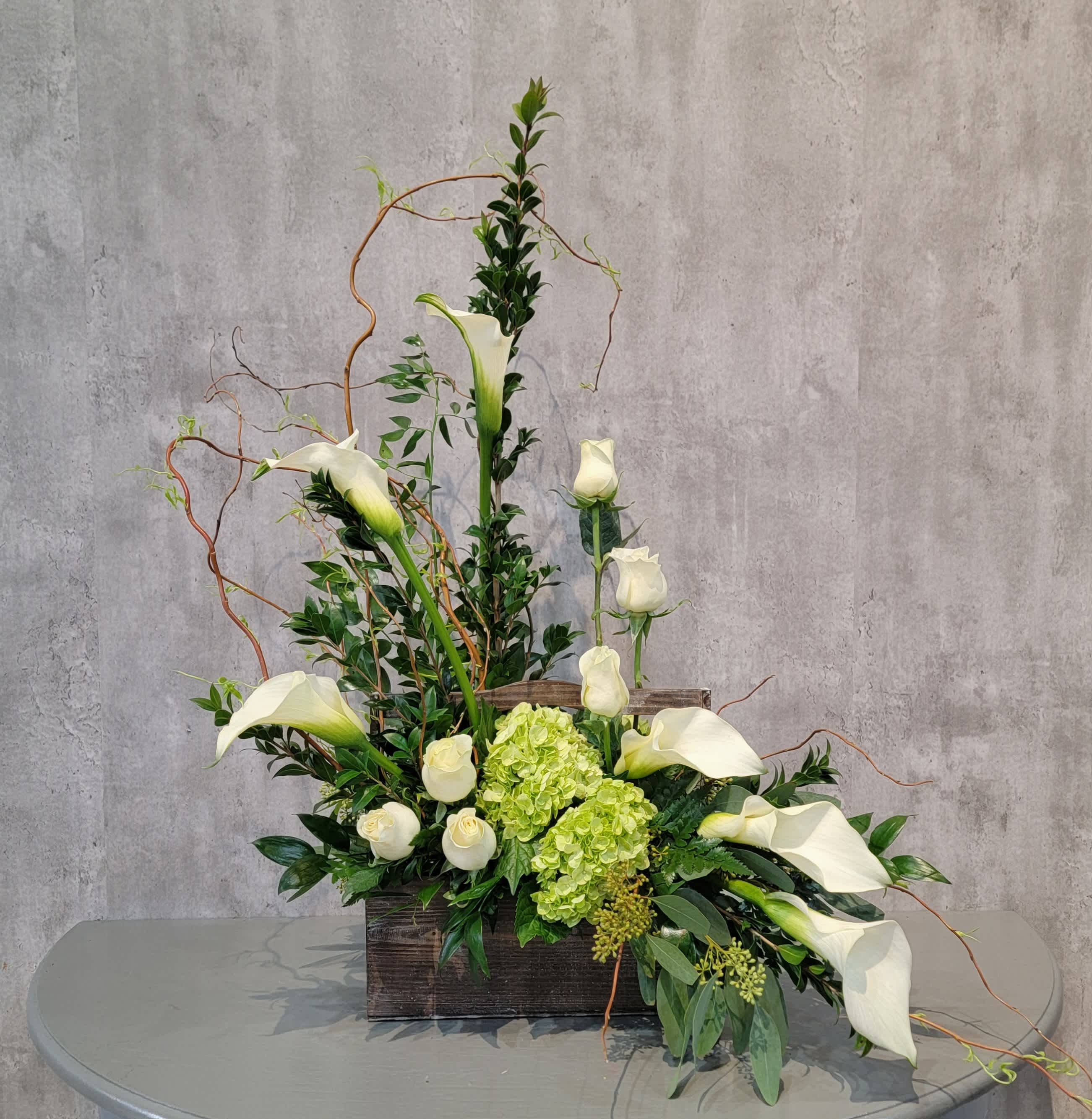 Tall floral arrangement with white calla lilies and green hydrangeas in a wooden box