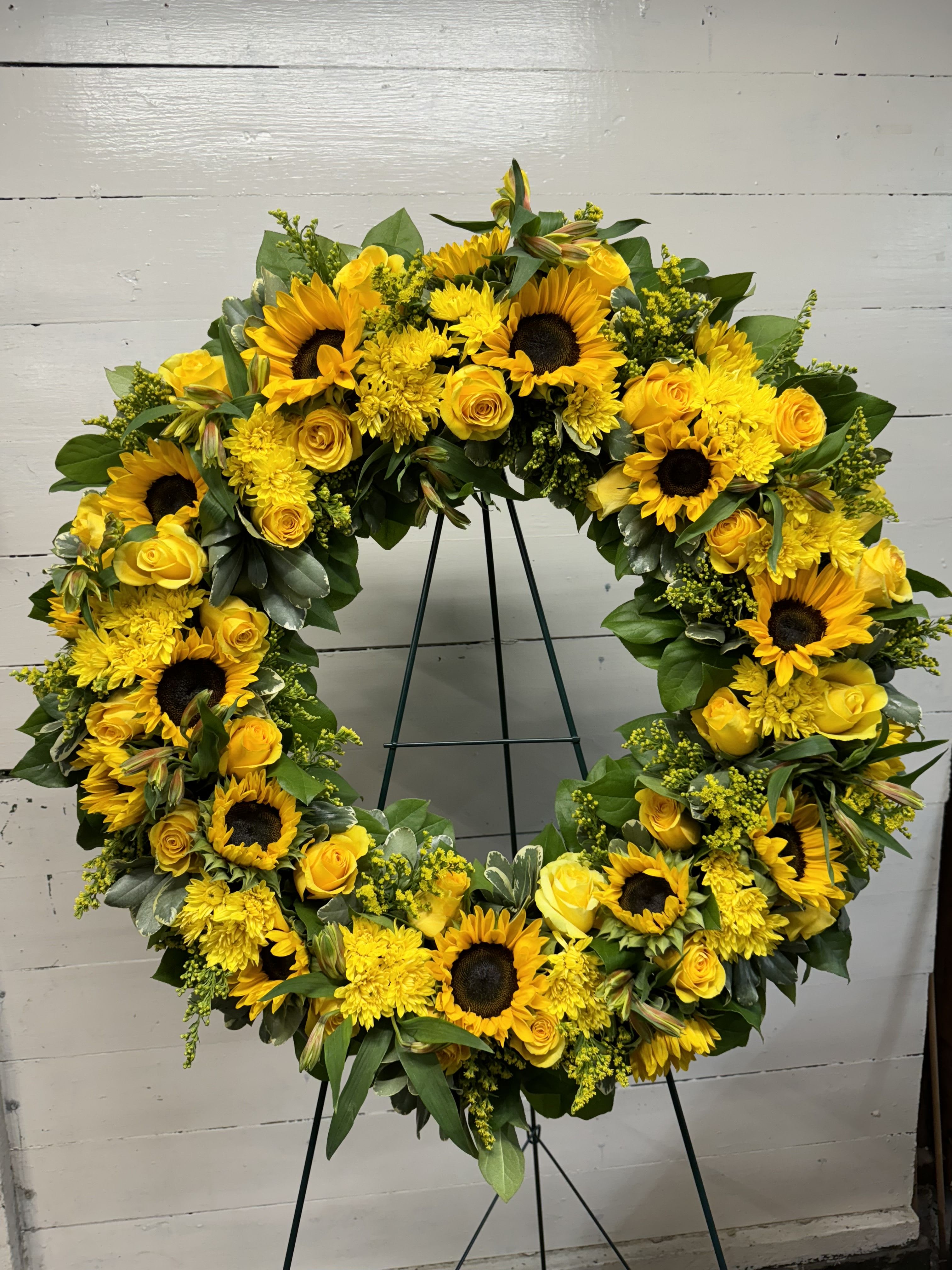 Large yellow floral wreath on a stand with sunflowers and roses