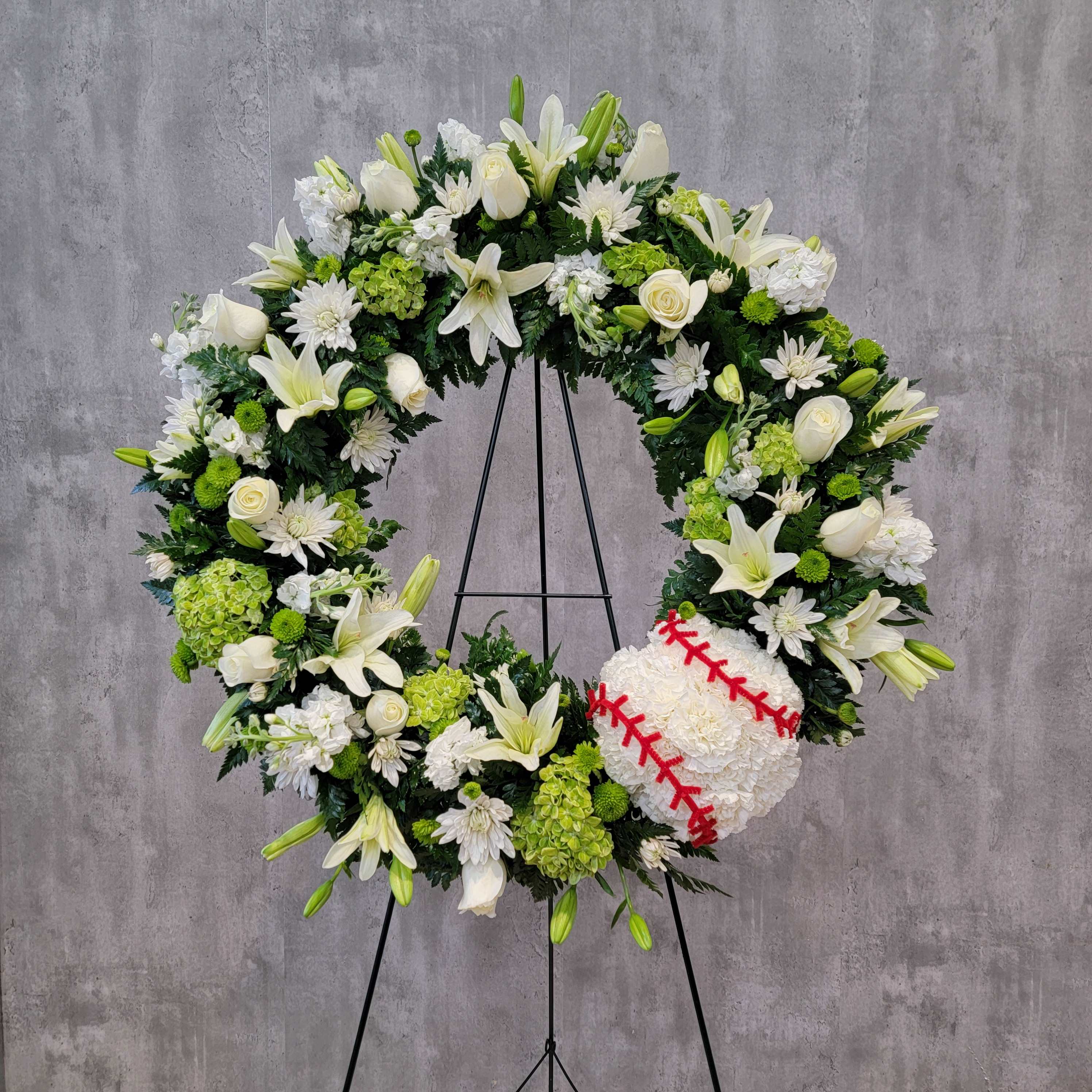 White floral wreath on a stand with a baseball at the lower right