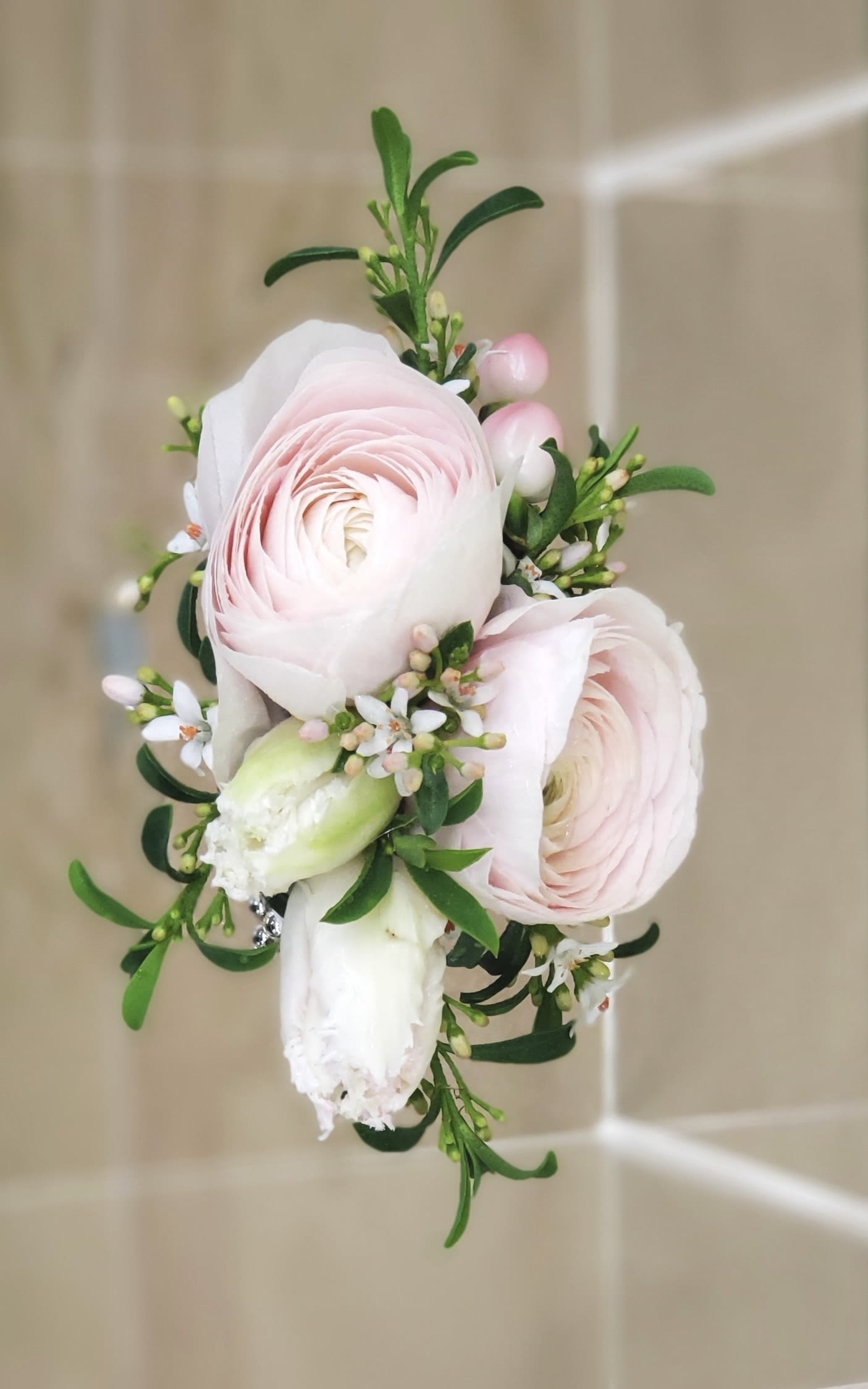 Pink ranunculus boutonniere with white blossoms and greenery