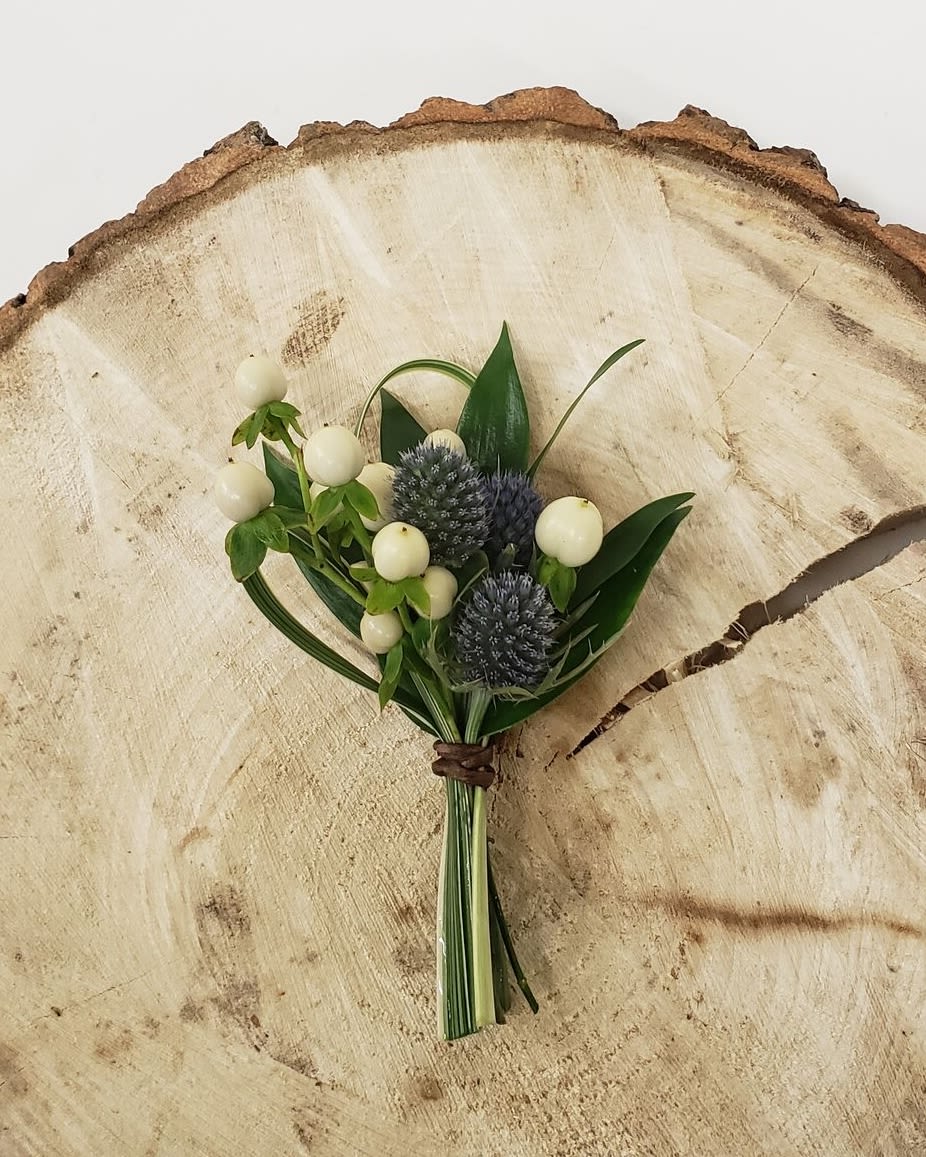Small boutonniere with white berries and blue thistle on a wood slice