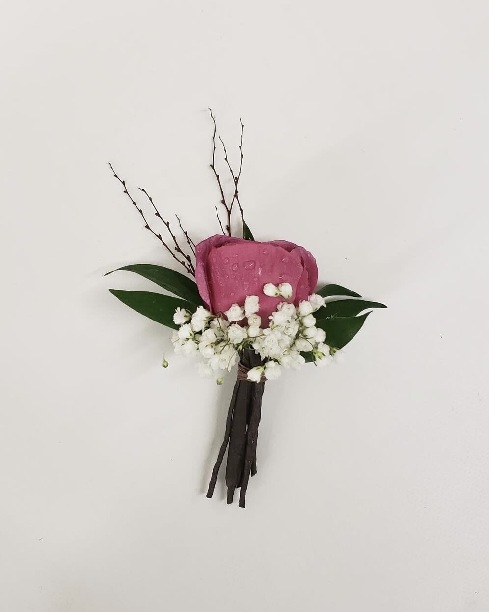 Pink rose boutonniere with white baby's breath and dark leaves