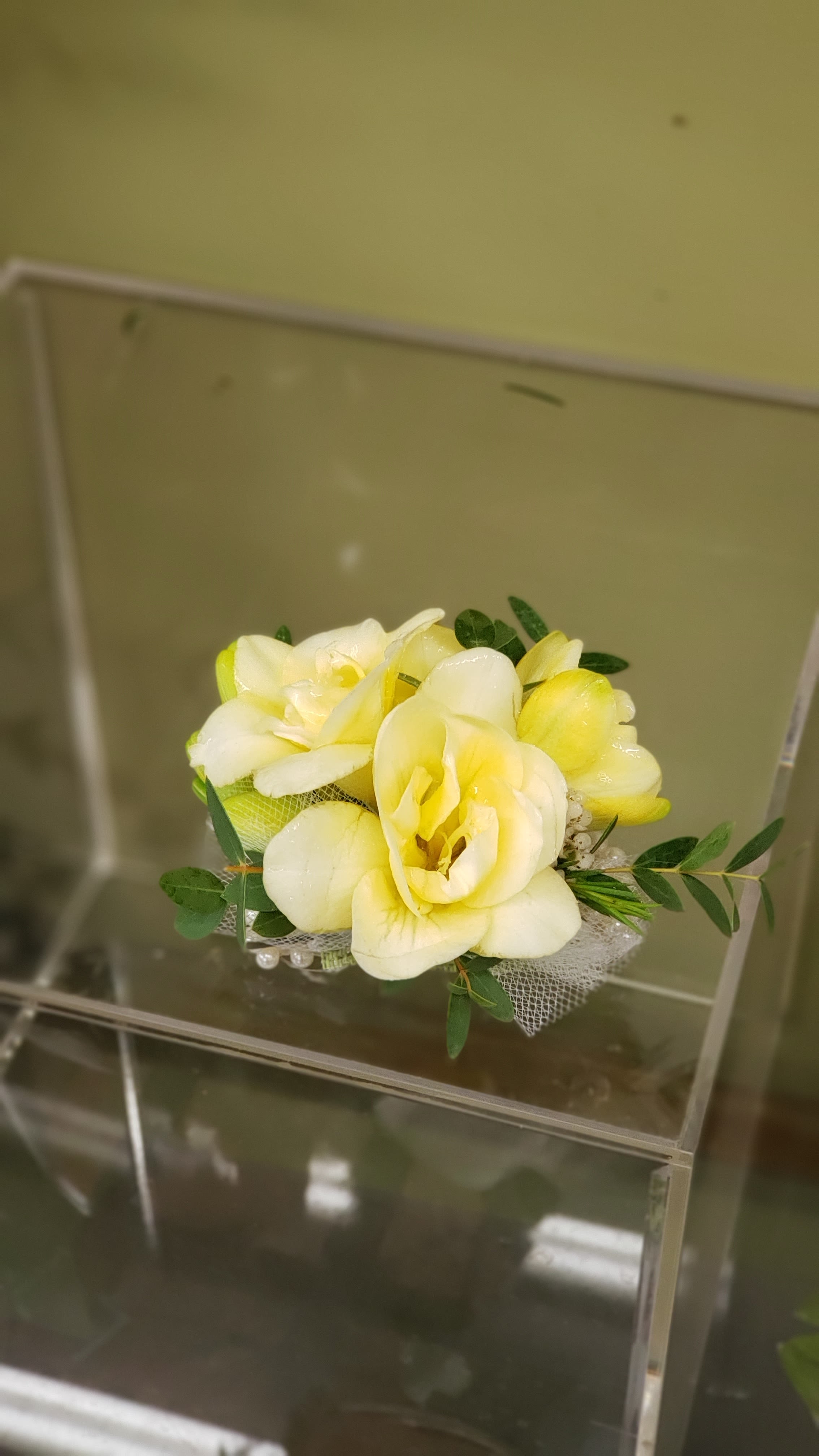 Small bouquet of pale yellow flowers with greenery and mesh wrap
