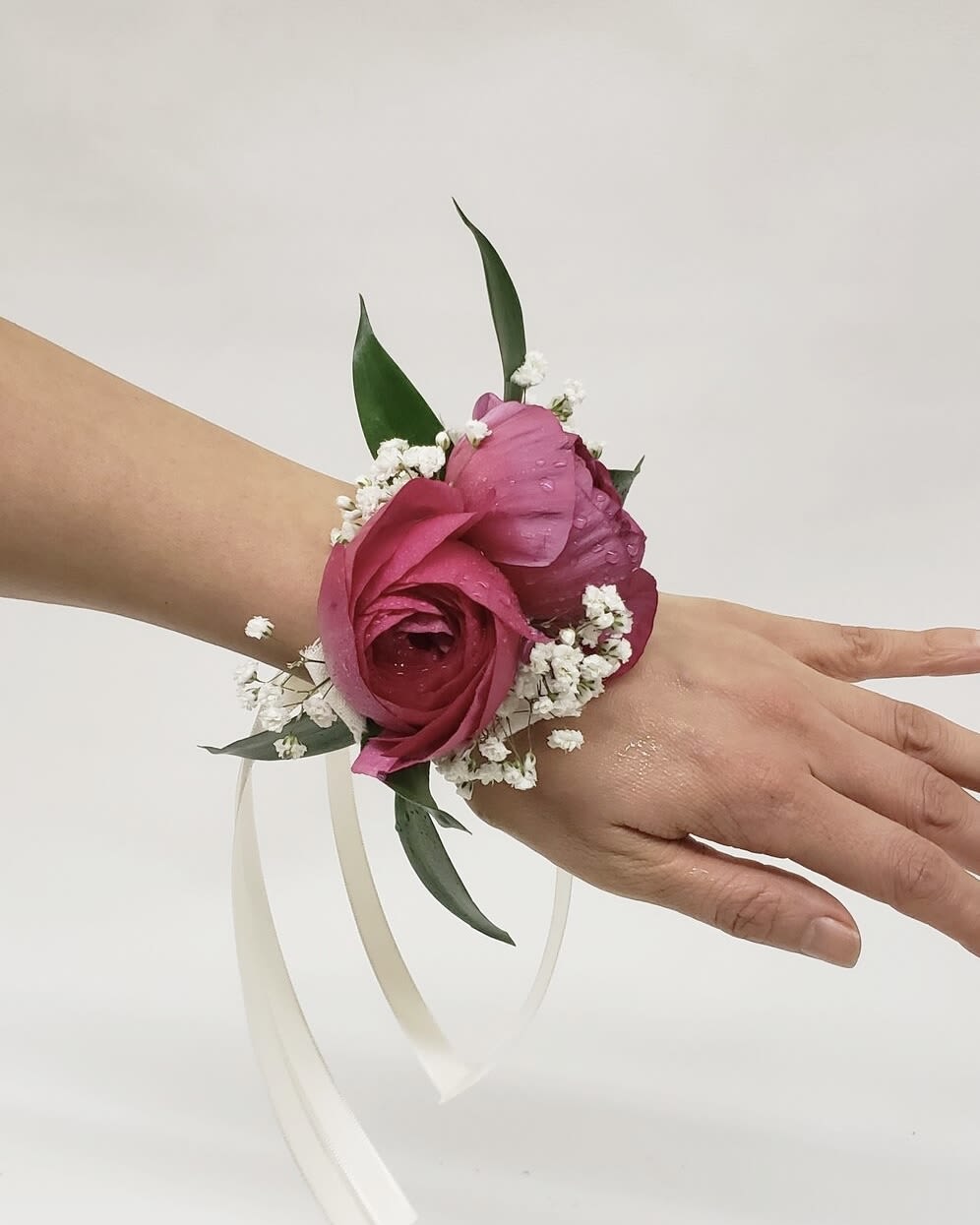 Pink floral wrist corsage with white baby's breath and ribbon