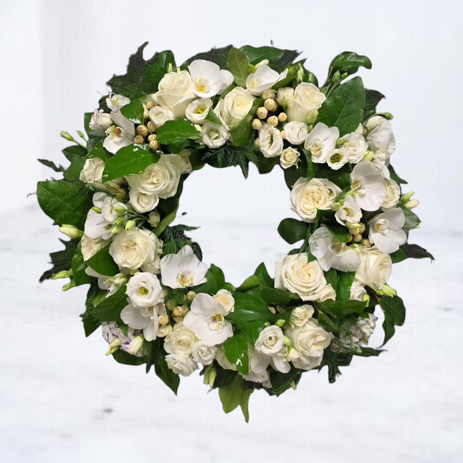 Vale Funeral Wreath - A serene tribute crafted in soft whites and rich green foliage, Vale Wreath offers a peaceful expression of remembrance. Designed at 18 inches in diameter and presented on a 48-inch stand, this elegant wreath features white roses, phalaenopsis orchids, lisianthus, and ivory berries. Each bloom is thoughtfully placed to create a lush, flowing circle that symbolizes eternal love and the continuity of life. A modern yet timeless floral tribute, ideal for funeral services, memorials, or celebrations of life.  white funeral wreath delivery Houston, modern sympathy wreath with orchids, all white rose wreath, elegant funeral flowers Houston TX, standing wreath for memorial, circular sympathy floral tribute  