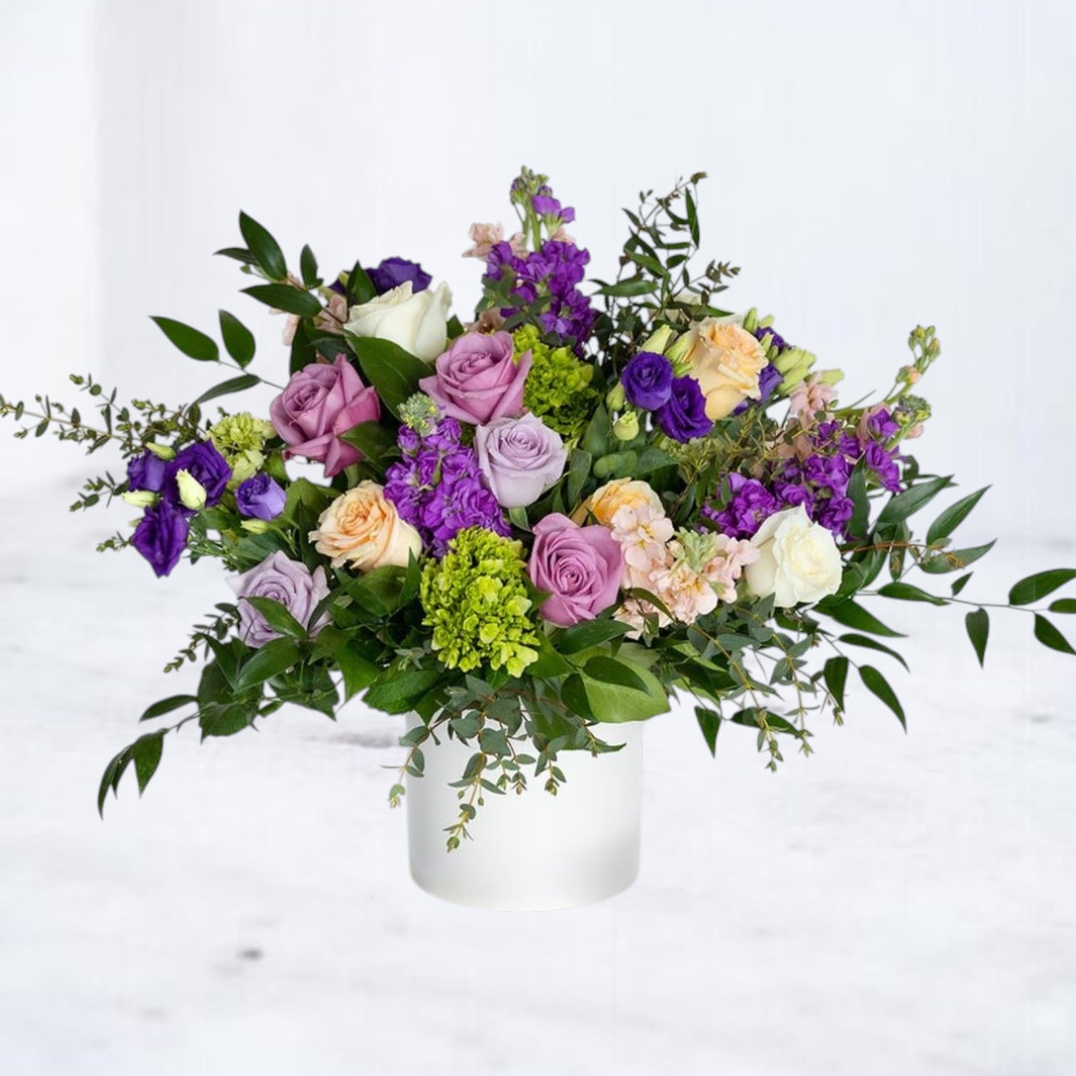 Dusktide - Dusktide is a graceful floral arrangement created to honor life with quiet beauty and depth. Designed in a matte white container, it features a thoughtfully curated blend of lavender, mauve, and peach roses, purple lisianthus, stock, green hydrangea, and lush seasonal greenery, offering texture, movement, and gentle color transitions.  Ideal for funeral services, memorials, or as a sympathy gift delivered to a loved one’s home. Its tone is refined and serene, a soft reflection of love, remembrance, and peace.  Same-day flower delivery available in Houston, TX, Willis, Plantersville, Magnolia, Montgomery, Porter and Spring