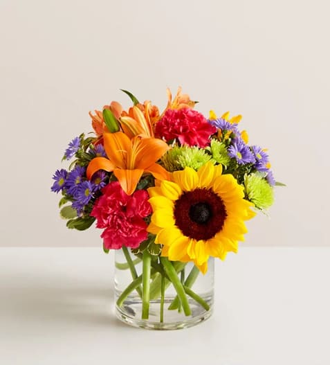 Colorful mixed bouquet in a clear glass vase with a sunflower and lilies