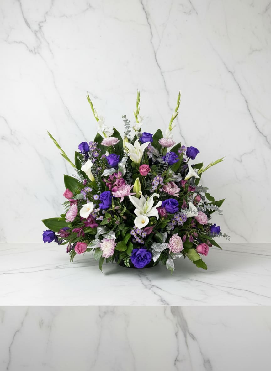 Violet Garden - A lush, garden-style arrangement featuring elegant white lilies and calla lilies surrounded by soft blush blooms and rich violet accents. Designed with layered greenery and airy texture, it brings a romantic, whimsical feel. 