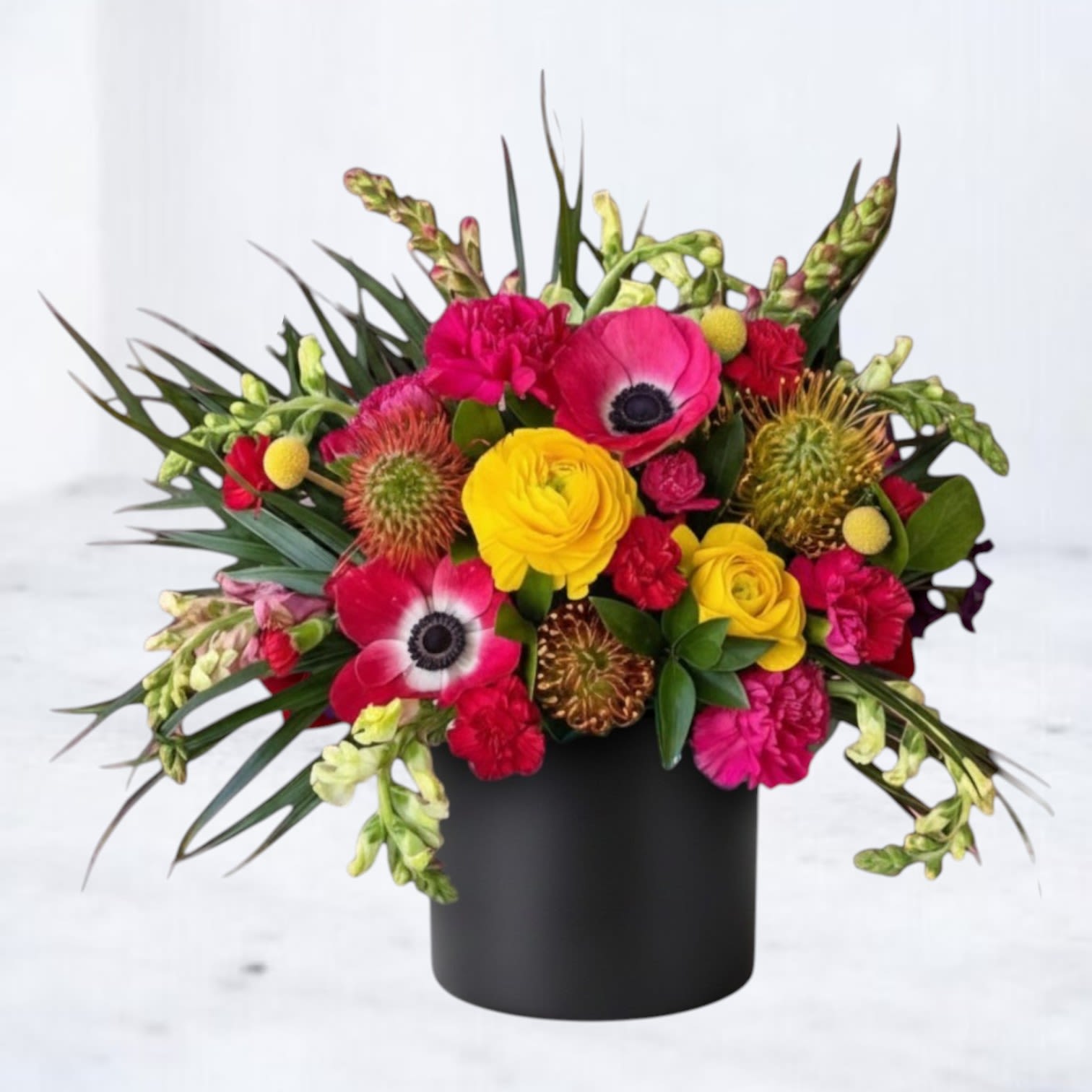Calyx - Calyx is a bold, modern floral arrangement designed with striking color contrast, sculptural texture, and dynamic movement. Featuring vibrant ranunculus, anemones, specialty blooms, and unique textural elements, this arrangement is artfully composed with structured greenery to create a dramatic, design-forward look.  Designed in a matte black vessel, Calyx blends saturated reds, hot pinks, and vivid yellows with deep green foliage for a composition that feels edgy, contemporary, and visually captivating. The combination of bold florals and spiky textures gives this arrangement a sculptural presence, making it a true statement piece.  Perfect for birthdays, celebrations, modern interiors, or sending something unexpected and unforgettable, this vibrant, high-impact flower arrangement is ideal for those who love unique, artistic floral design.  Same-day flower delivery is available in Magnolia, TX, The Woodlands, Montgomery, Conroe, Spring, Tomball, and surrounding North Houston areas.  Due to seasonal availability, some blooms may be replaced with similar varieties of equal or greater value to maintain the design’s look and integrity. Your arrangement will always reflect the same color palette, style, and premium quality.