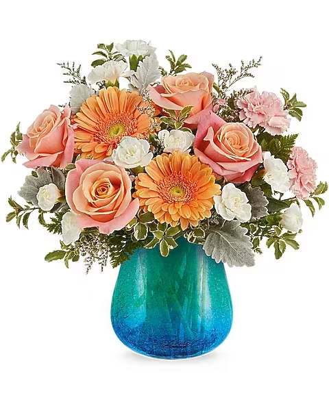 Ocean Sunrise Bouquet - Capture the glow of morning light with the Ocean Sunrise Bouquet, a breathtaking blend of coral, peach, and pink blooms displayed in a turquoise glass vase featuring a soft crackled texture and soothing color gradient.