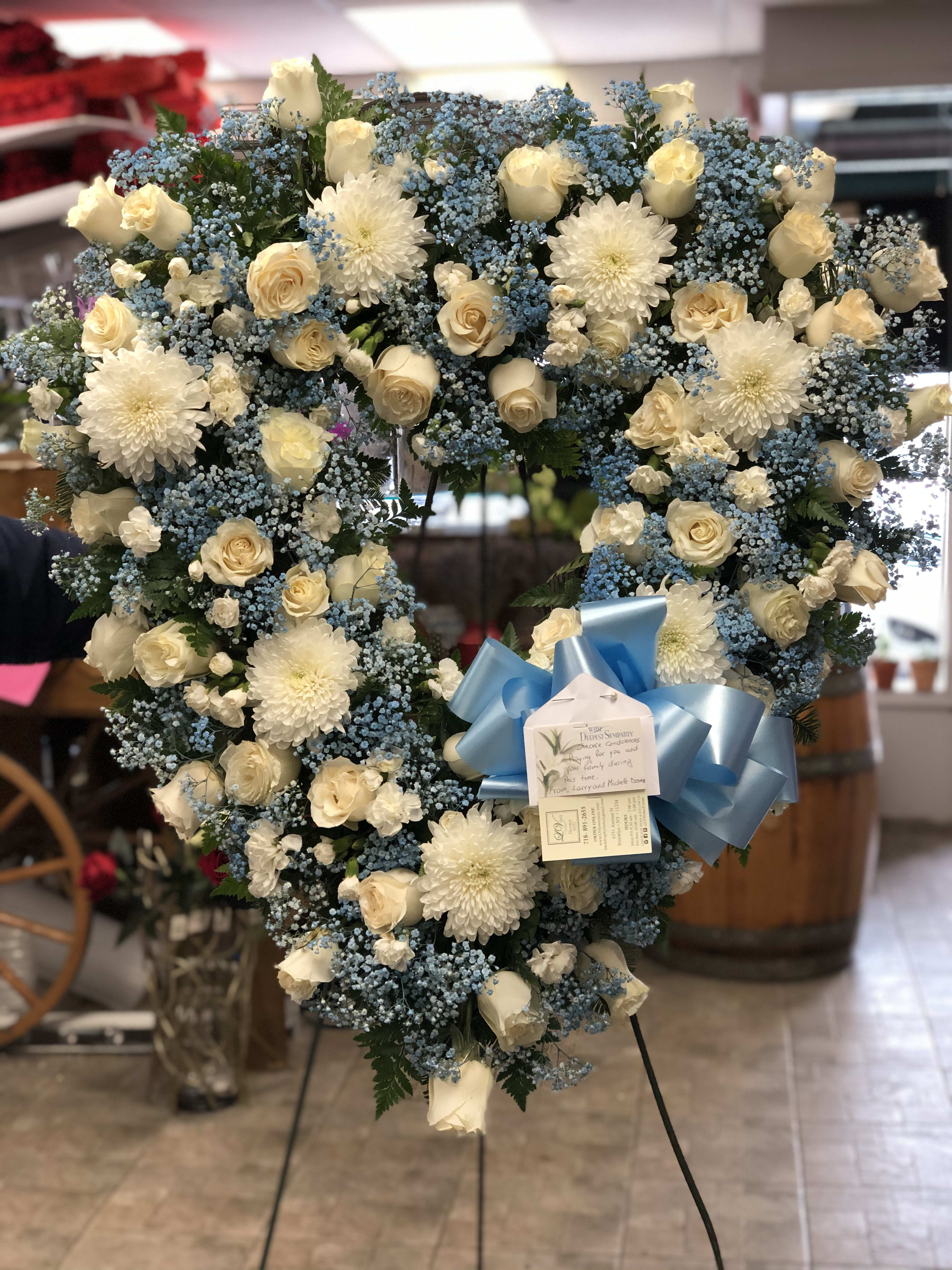 Heart-shaped floral wreath of white roses and blue filler flowers with a blue bow