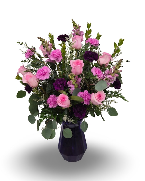 Lucky in Love - Lucky in Love is a lush and romantic arrangement featuring soft pink roses, rich purple blooms, and layers of fresh greenery for a beautifully balanced and elegant look. Designed with graceful movement in a faceted glass vase, this arrangement makes a striking statement while still feeling warm and inviting. Measuring approximately 28 inches tall by 21 inches wide, it’s a stunning way to celebrate love, joy, and meaningful moments.