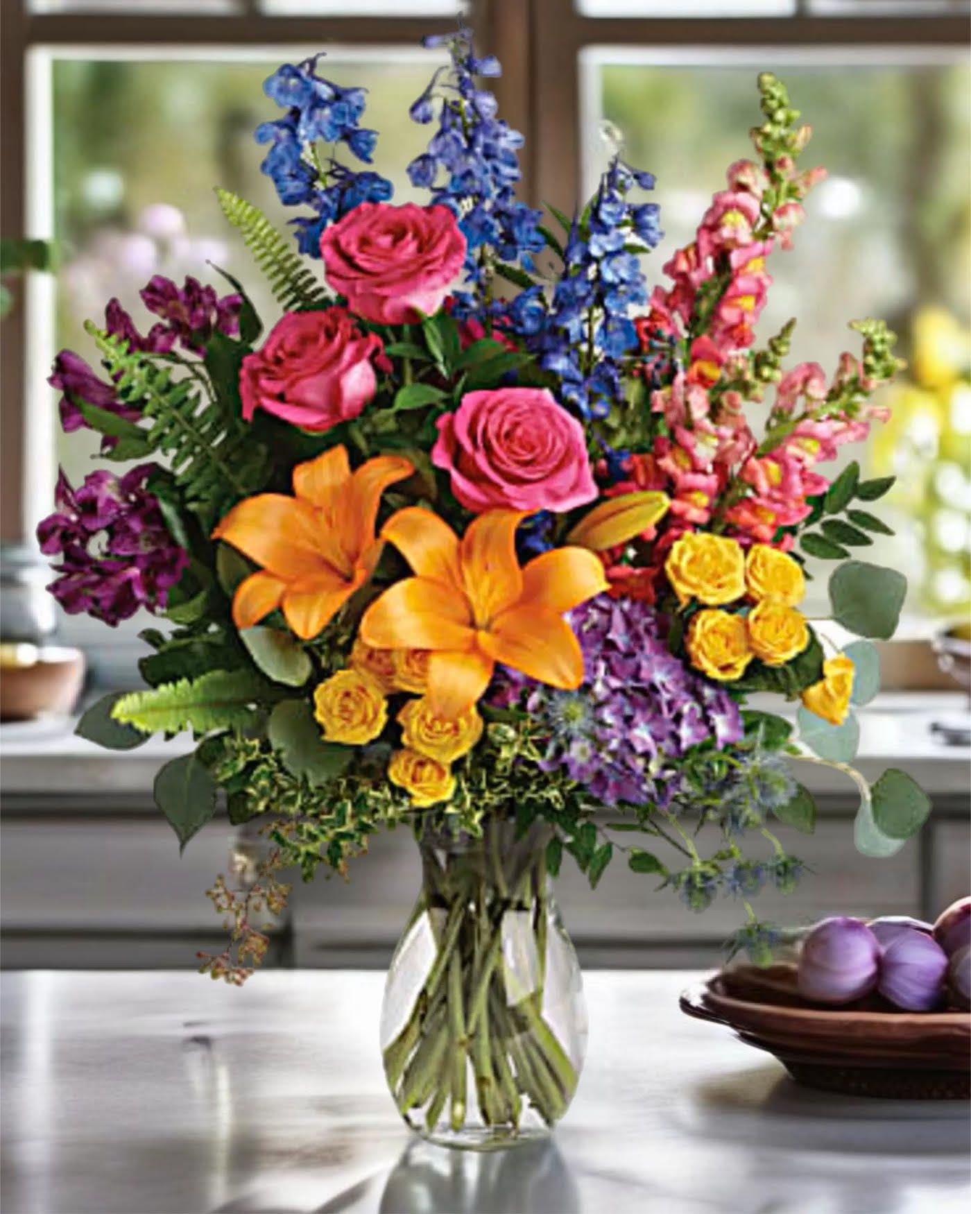 Colorful bouquet of roses, lilies, and snapdragons in a clear glass vase