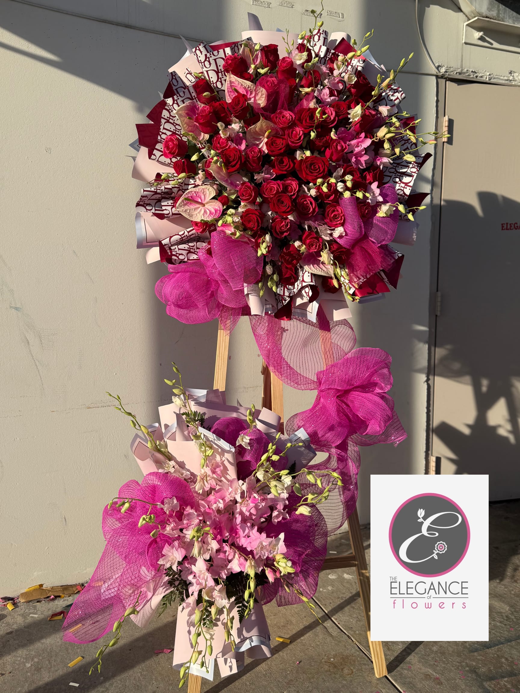 Large standing floral display of red roses and pink flowers with magenta ribbon