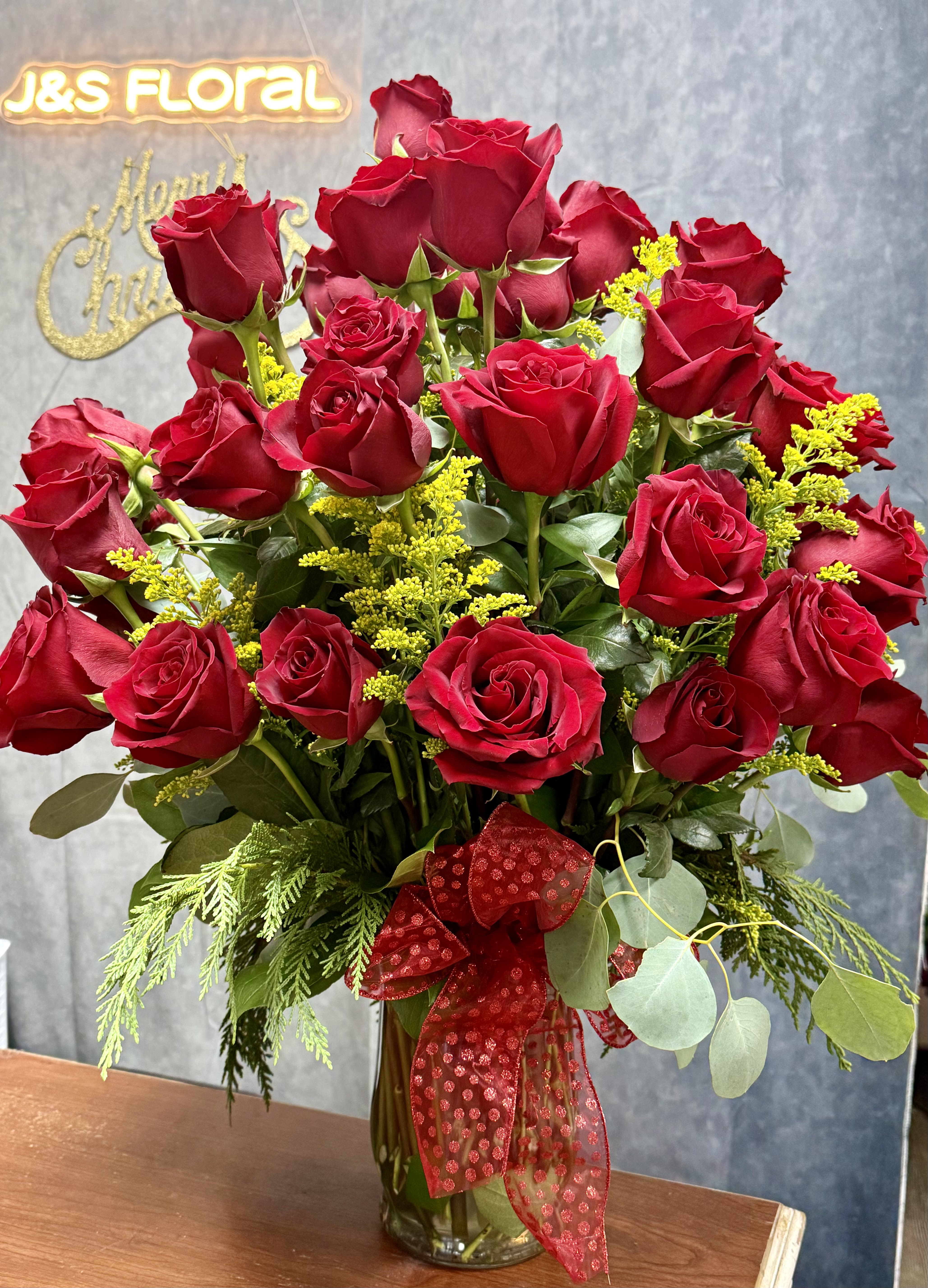 Red roses arranged in a glass vase with a red ribbon