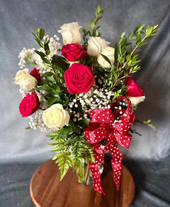 Bouquet of red and white roses with baby's breath and a red polka-dot ribbon in a glass vase