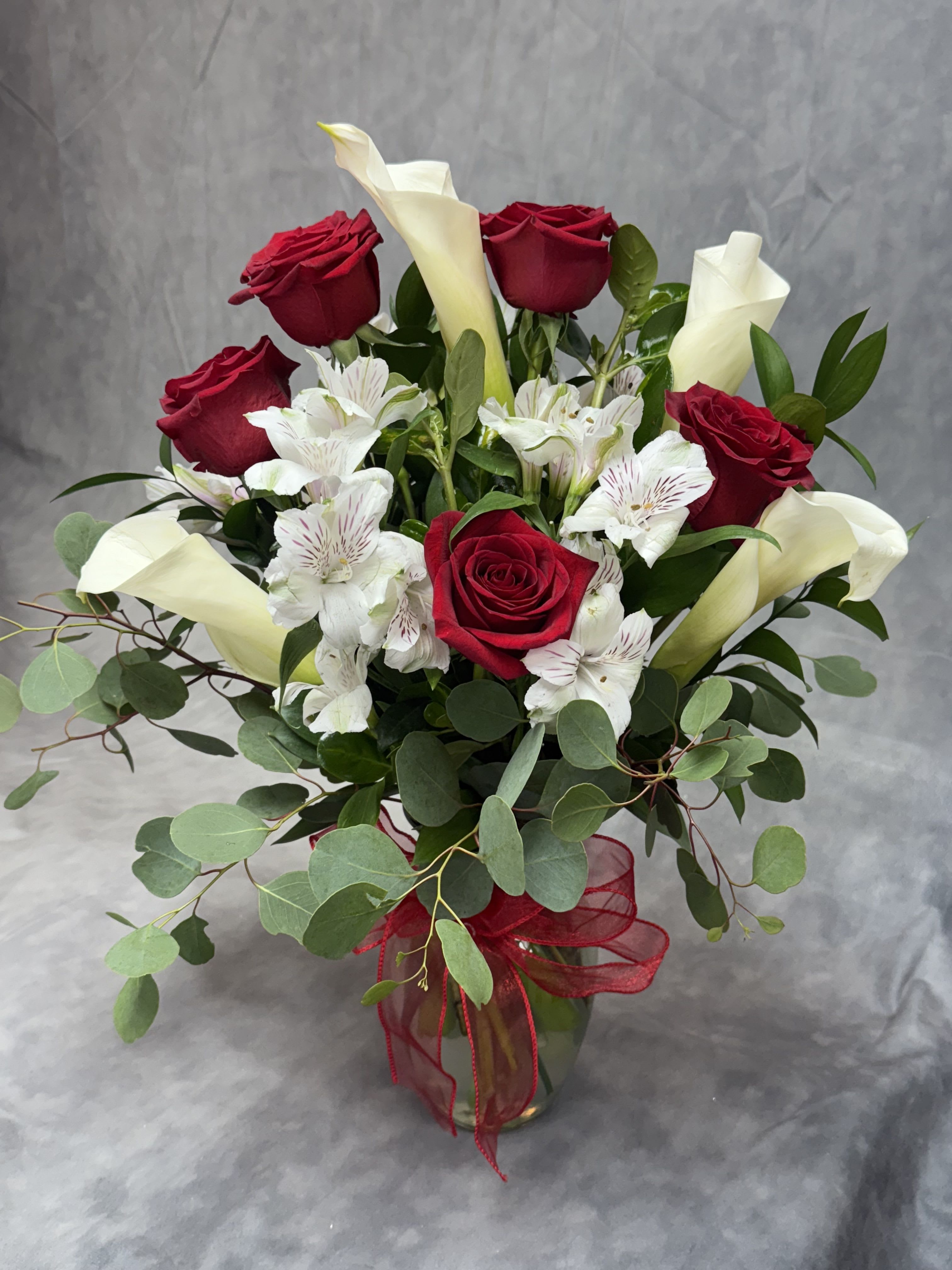 Bouquet of red roses, white calla lilies, and white alstroemeria in a glass vase