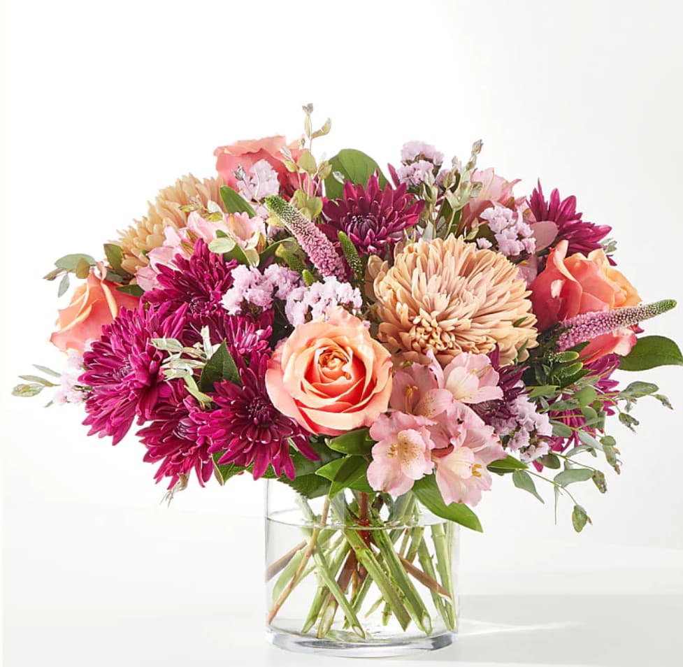 Mixed bouquet of pink, peach, and purple flowers in a clear glass vase