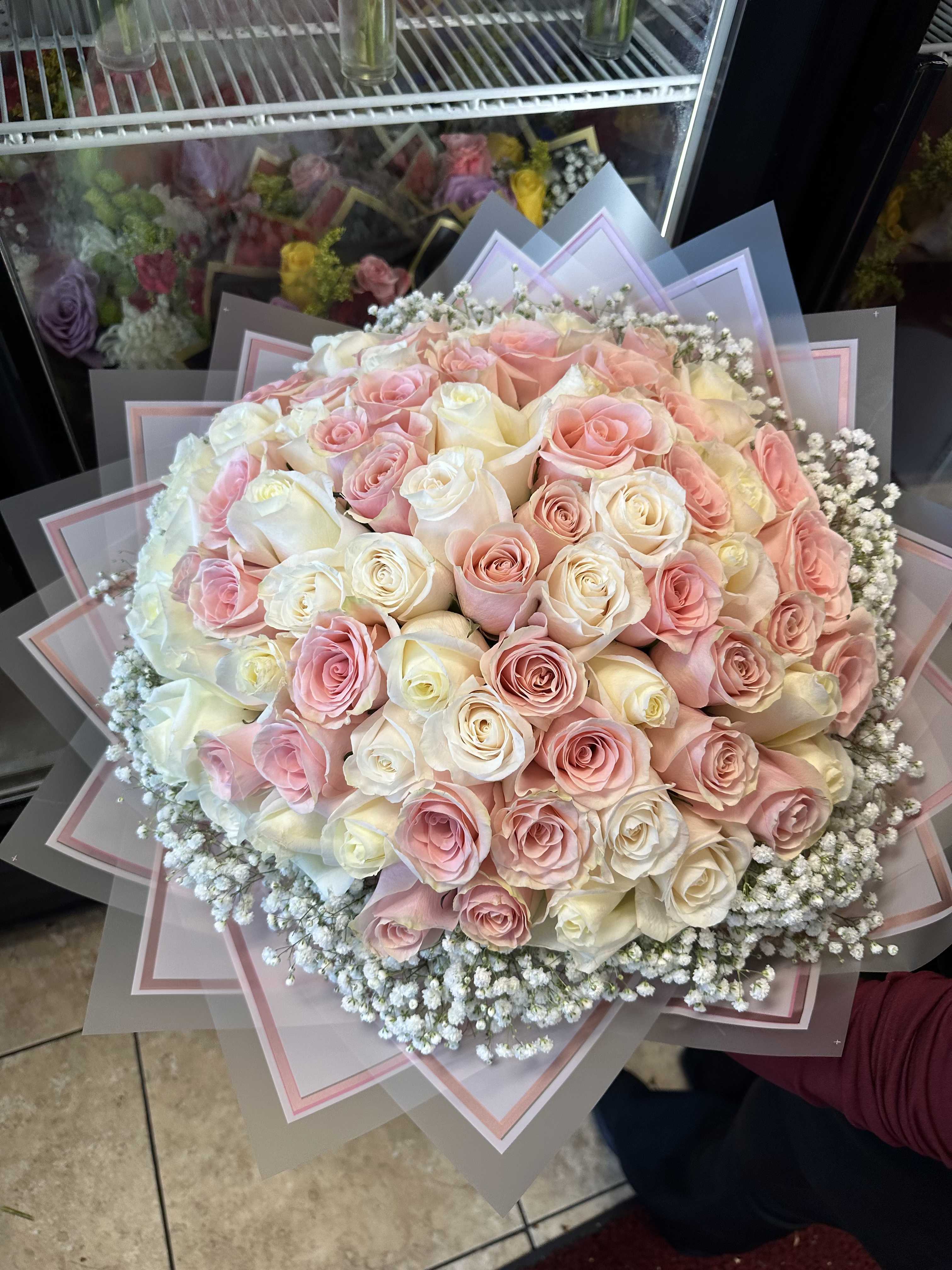 Pink Love - A lush dome of pale pink, blush and creamy white roses creates an instant sentiment - this flower arrangement is a romantic birthday bouquet and a tender choice for Mother's Day or an anniversary. The tightly clustered roses form a full, soft head that reads as both elegant and deeply affectionate, the kind of gift that makes the person you're thinking of feel truly cherished.  Delicate white filler flowers halo the rose cluster, adding a fine, airy texture that softens the silhouette and enhances the pastel palette. The stems are finished in multiple layers of frosted and pink-edged decorative wrapping paper, folded into star-like points for a structured, luxury presentation that looks beautiful on arrival. Size is generous: a large, dome-shaped head designed to impress without being fussy.  Perfect for birthdays, expressions of love and romance, or to celebrate Women's Day and Best Friends Day, this bouquet reads as a warm, personal gesture. Arrange for delivery to make someone feel seen and adored; to keep the roses looking their best, trim stems and refresh water daily once received.