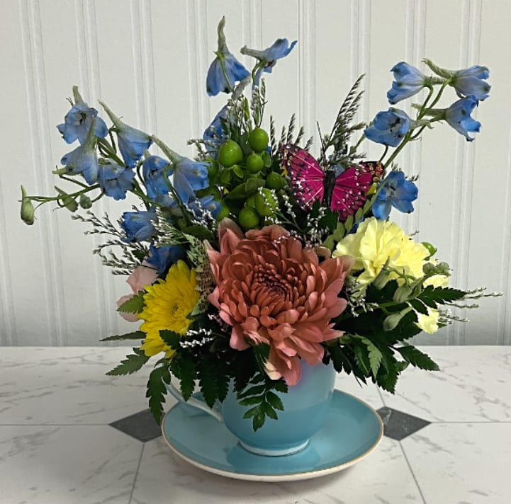 Tea Time - A charming arrangement served with a touch of whimsy. Tea Time is designed in a small turquoise teacup and features a soft mix of blue, green, yellow, pink, and peach blooms, accented with a delicate butterfly. It’s the perfect petite gift for tea lovers, spring celebrations, or a sweet surprise just because.