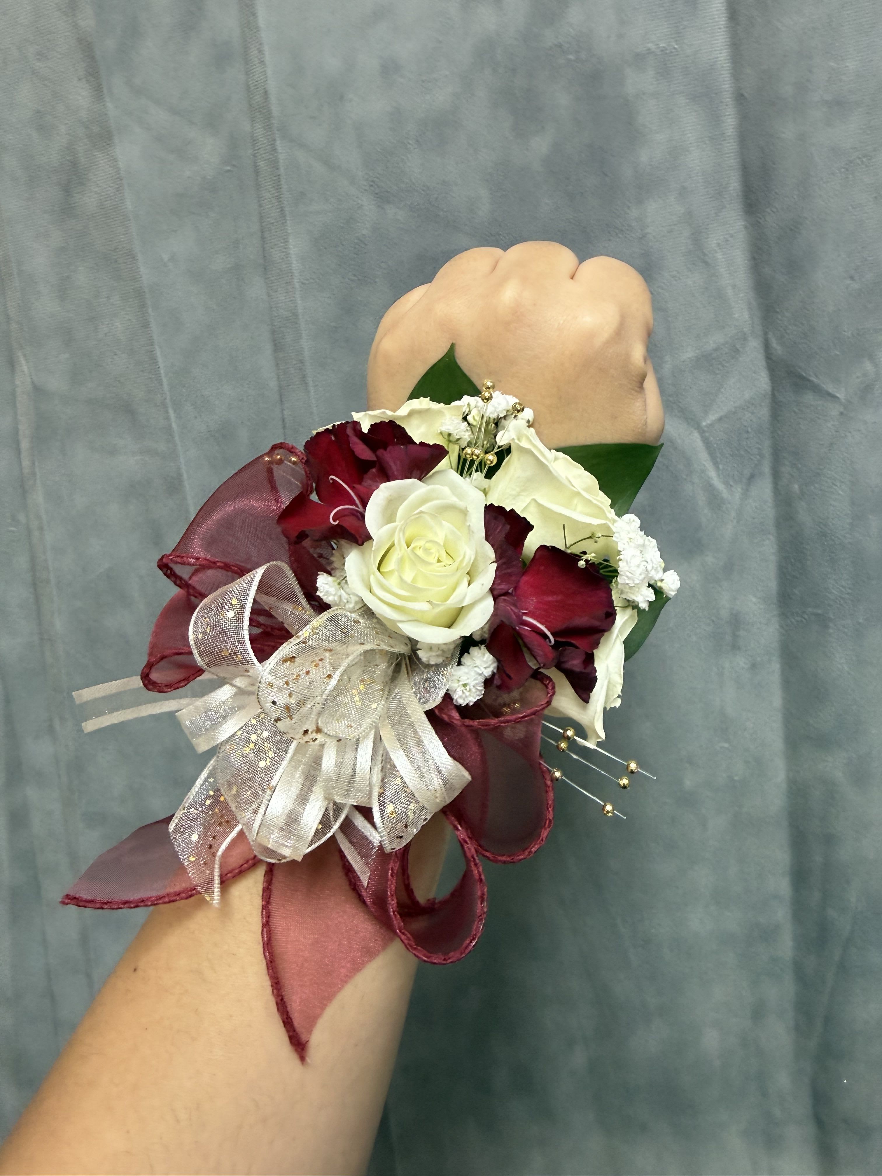 White burgundy wrist corsage - White spray roses and burgundy mini carnation with gold accents, finished with a layered sheer and burgundy ribbon bow with pearl wrist band 