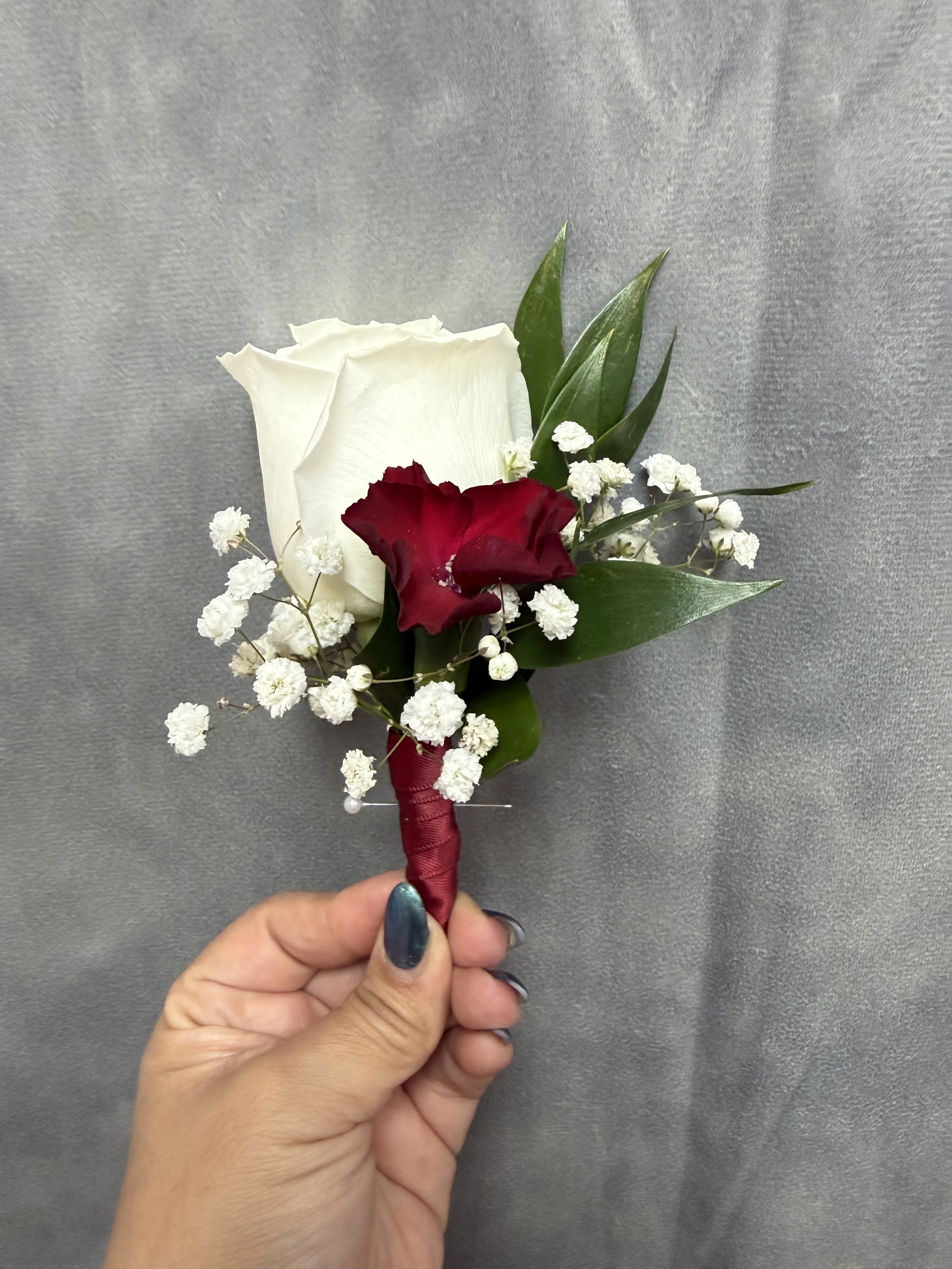 White burgundy boutonnière  - White rose and deep red mini carnation boutonnière with baby's breath and greenery, wrapped in burgundy ribbon
