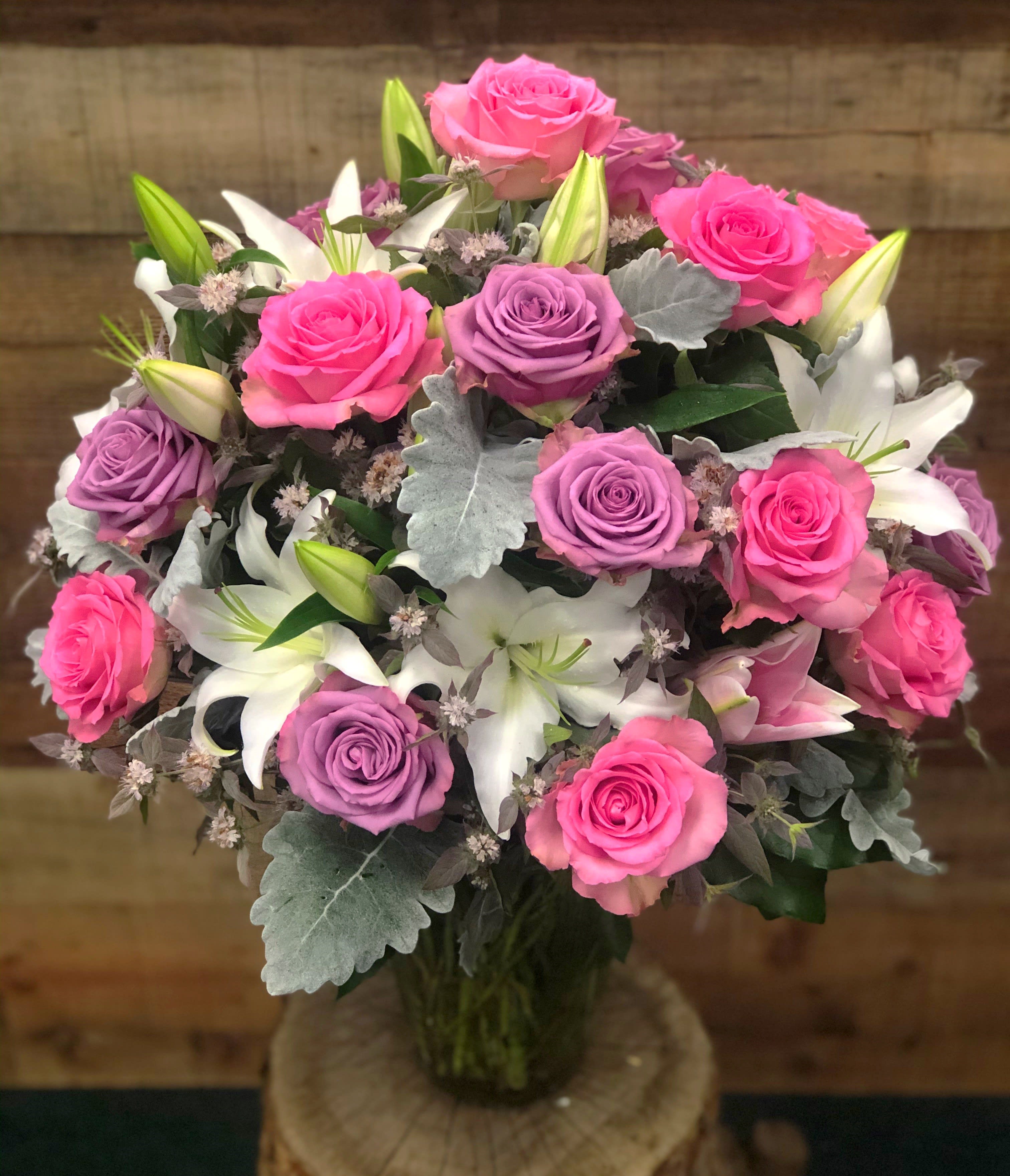 Bouquet of pink and lavender roses with white lilies in a glass vase