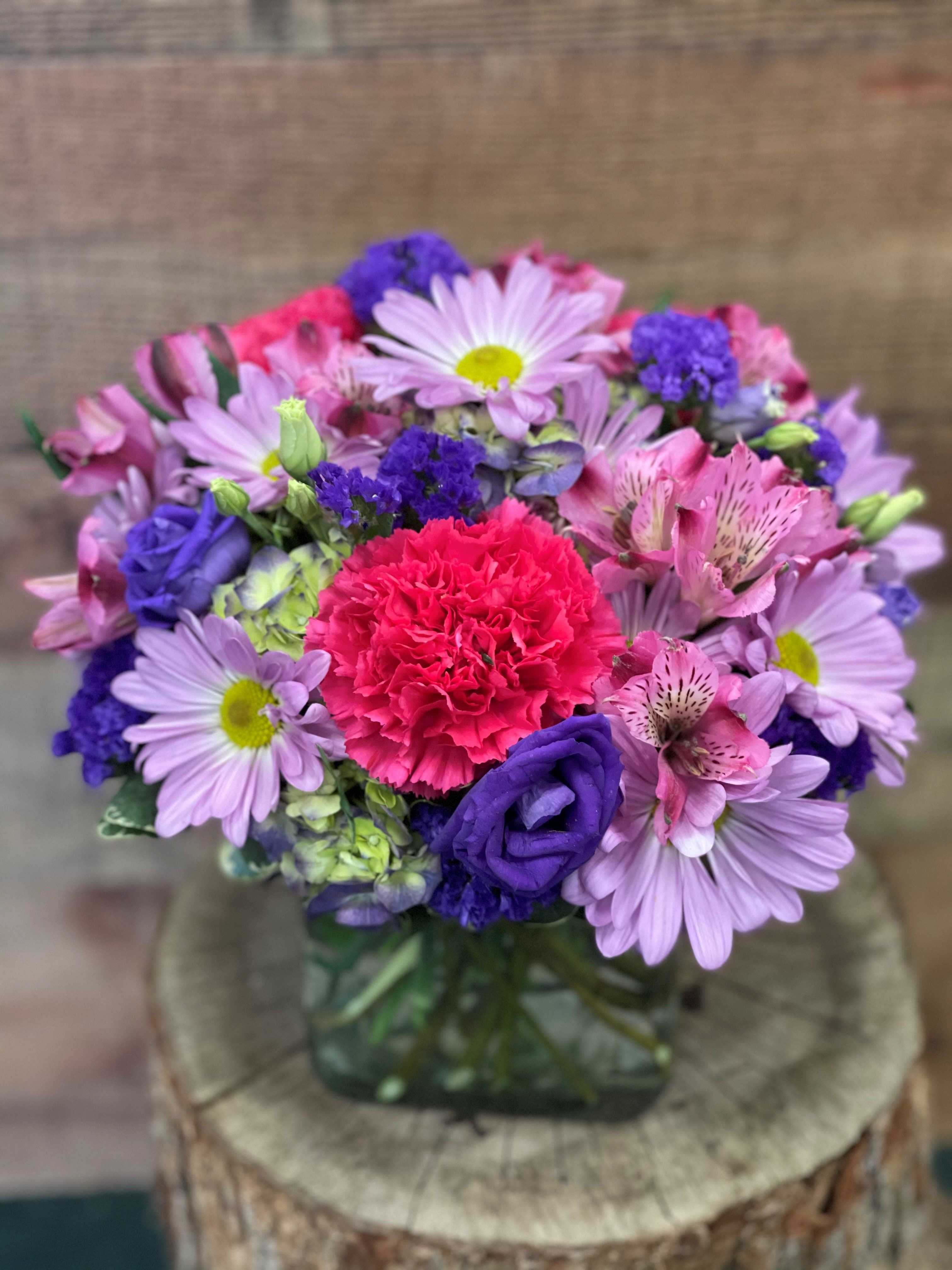 Mixed bouquet of pink, purple, and lavender flowers in a glass vase