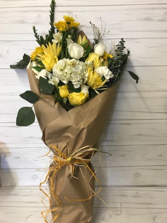 Yellow and white bouquet wrapped in brown paper with a raffia tie