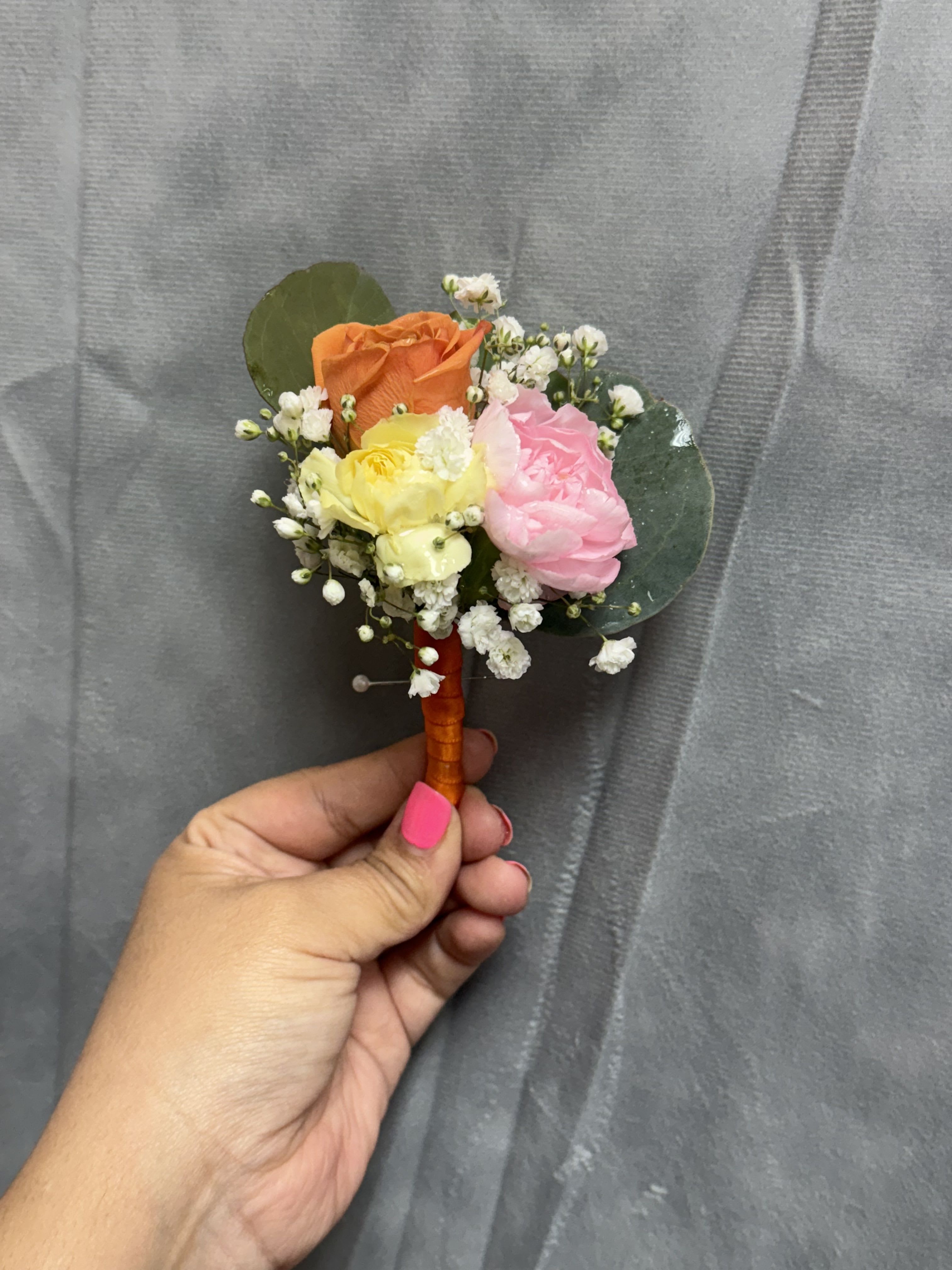 Orange yellow pink boutonnière  - Three small roses in orange spray rose , mini yellow and mini pink carnations with white filler and greenery , stems wrapped with orange ribbon 